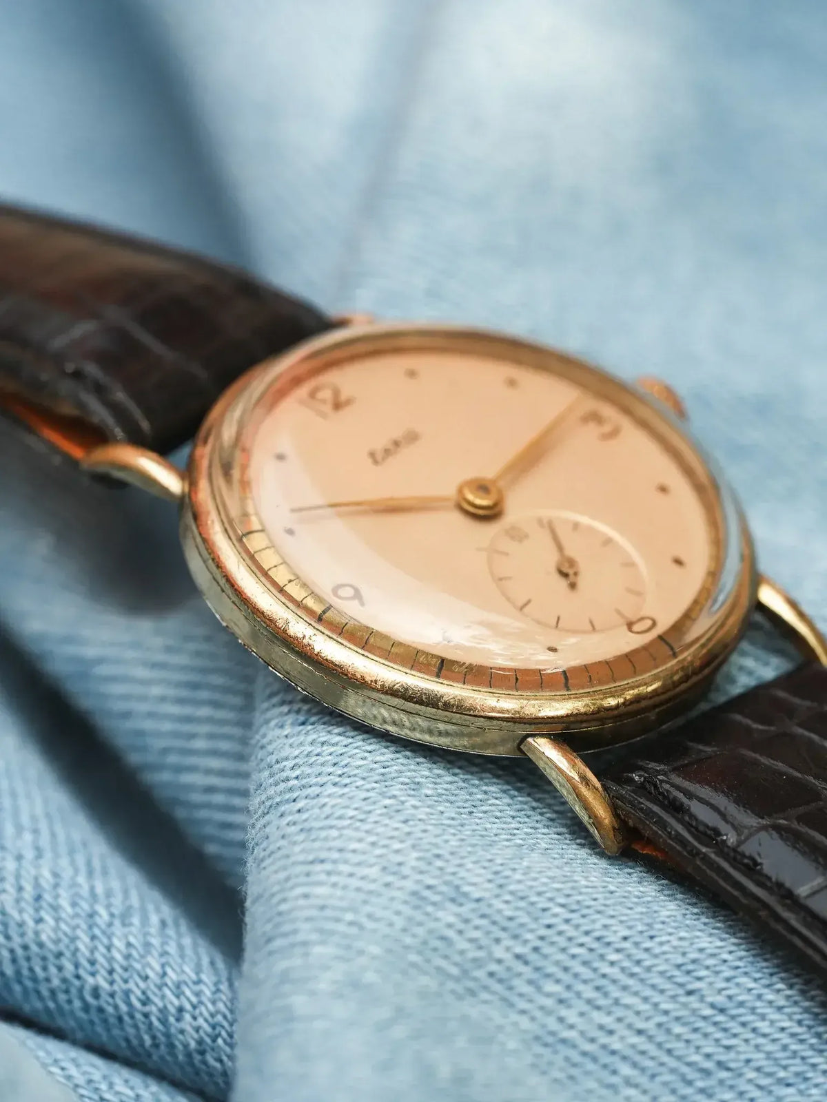 Vintage Longines watch with gold case, cream dial, and brown alligator strap on denim