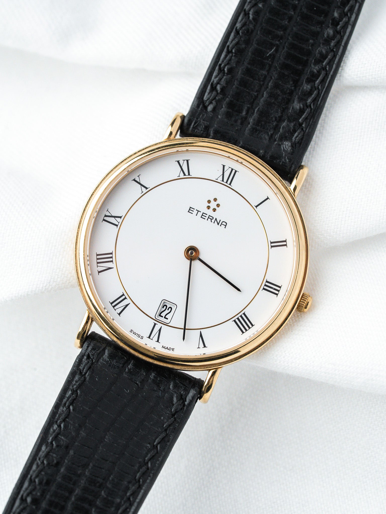 Eterna vintage watch with gold case, white dial, Roman numerals, black leather strap