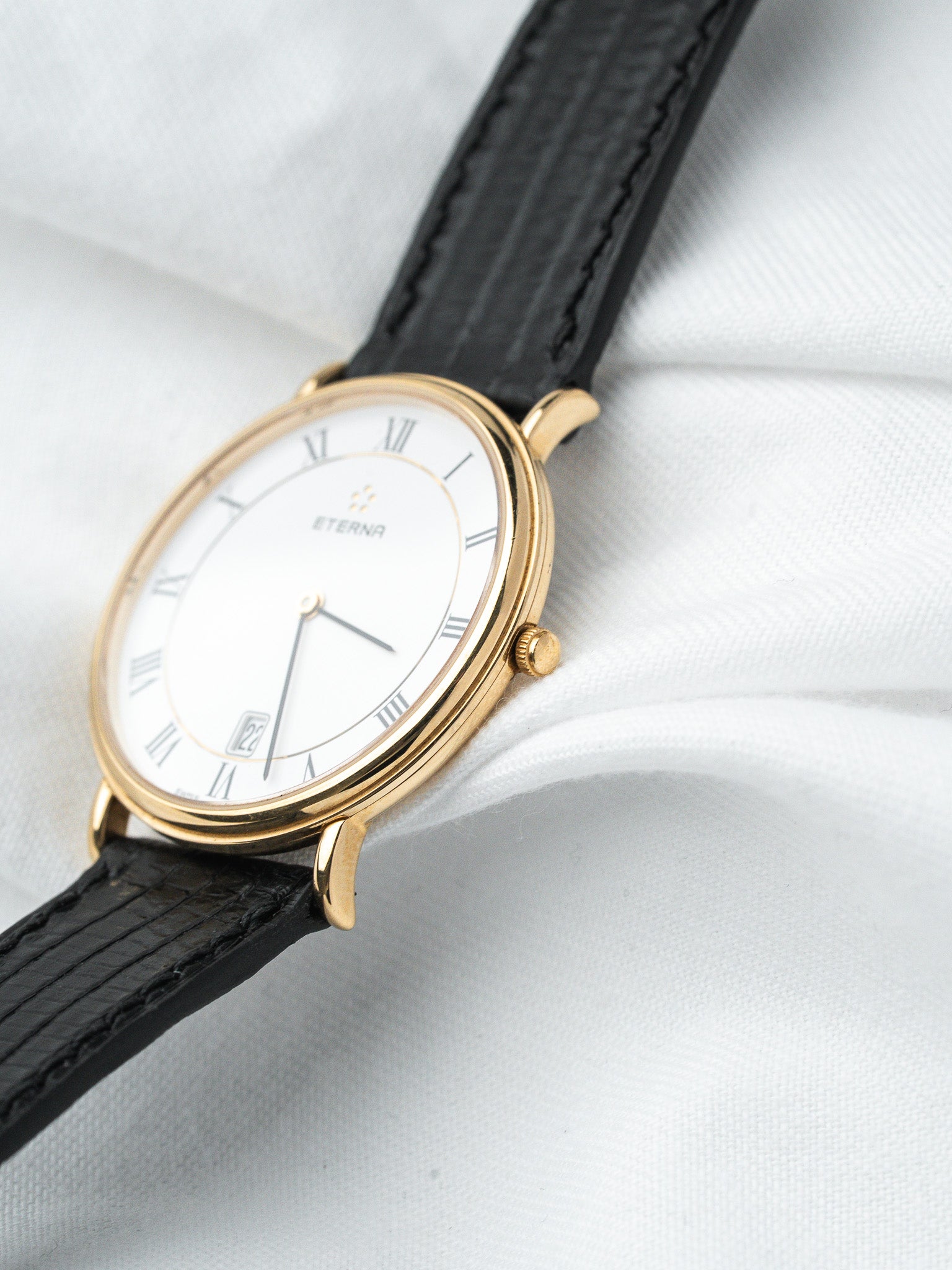 Eterna vintage watch with gold case, white dial, Roman numerals, black leather strap