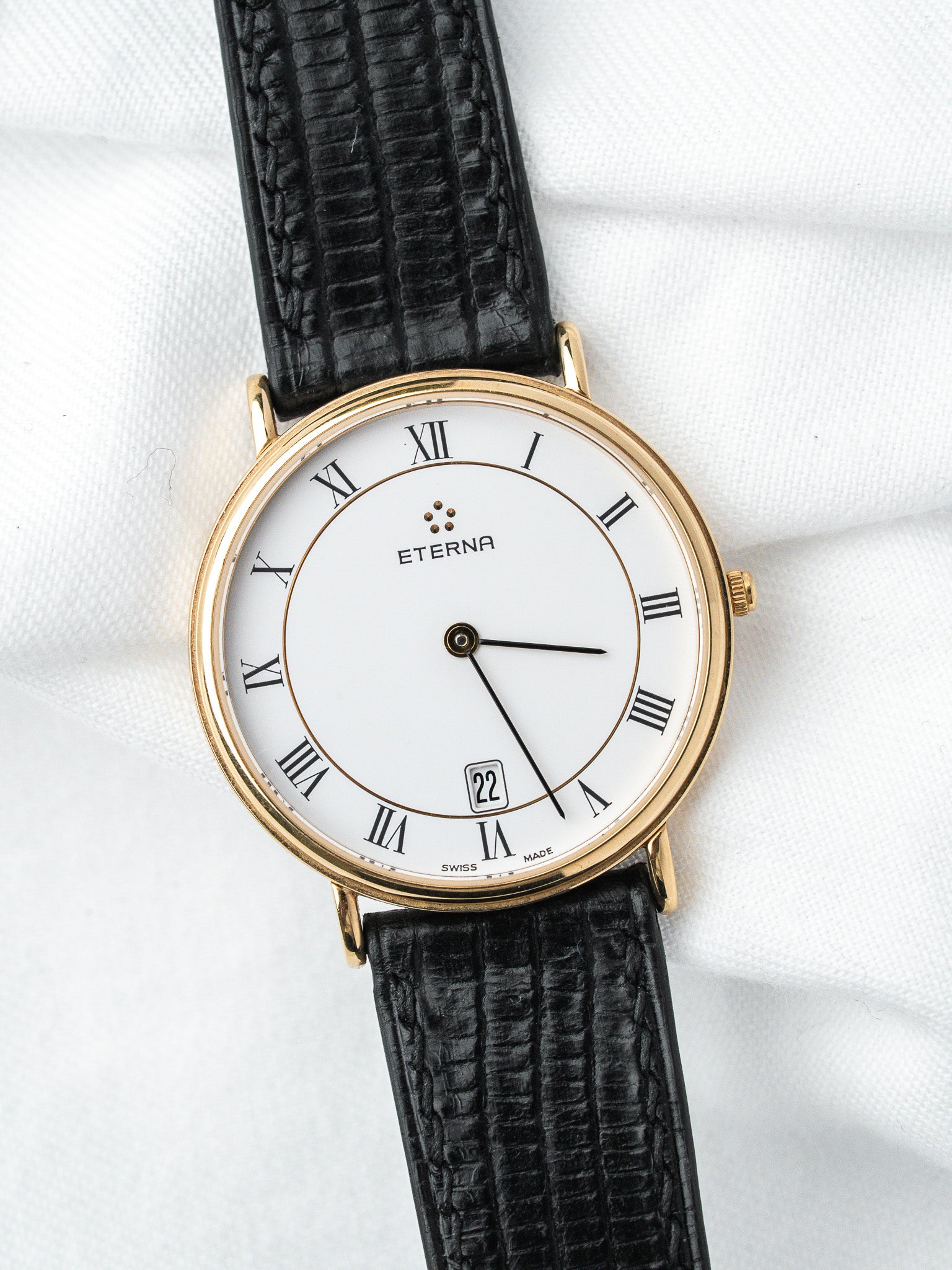 Eterna vintage watch with gold case, white dial, Roman numerals, and black leather strap