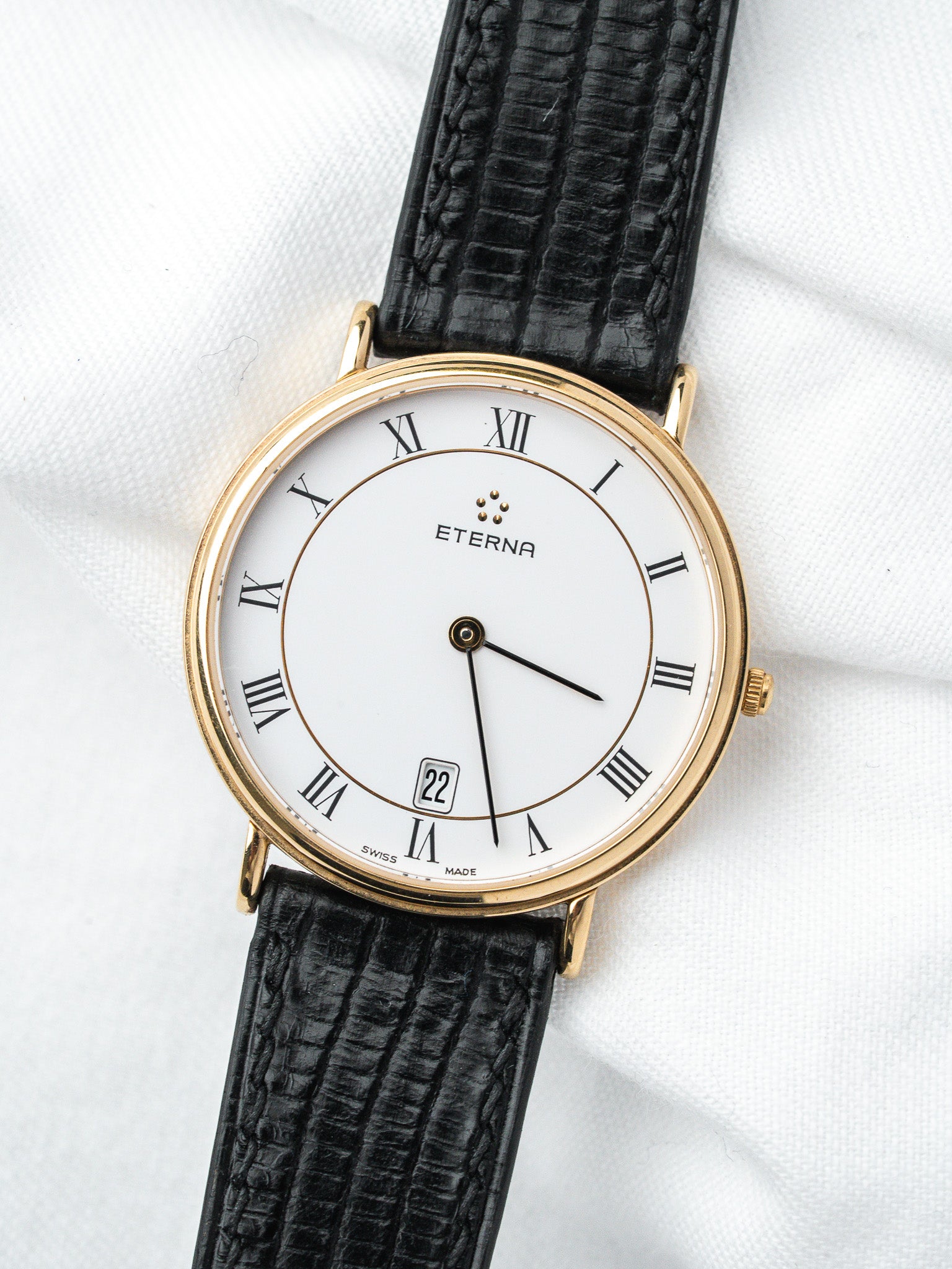 Eterna vintage watch with gold case, white dial, Roman numerals, black leather strap
