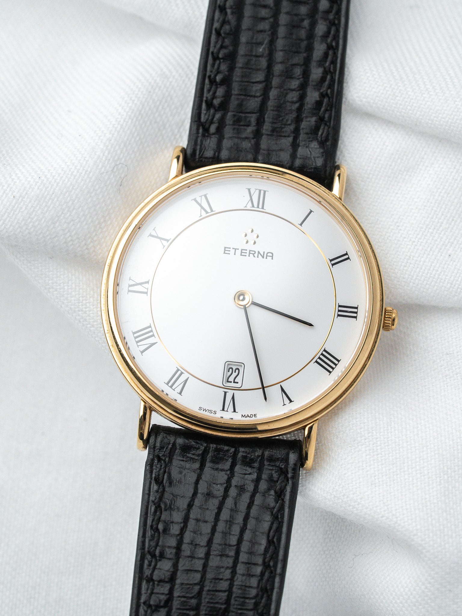 Eterna vintage watch with gold case, white dial, Roman numerals, and black leather strap