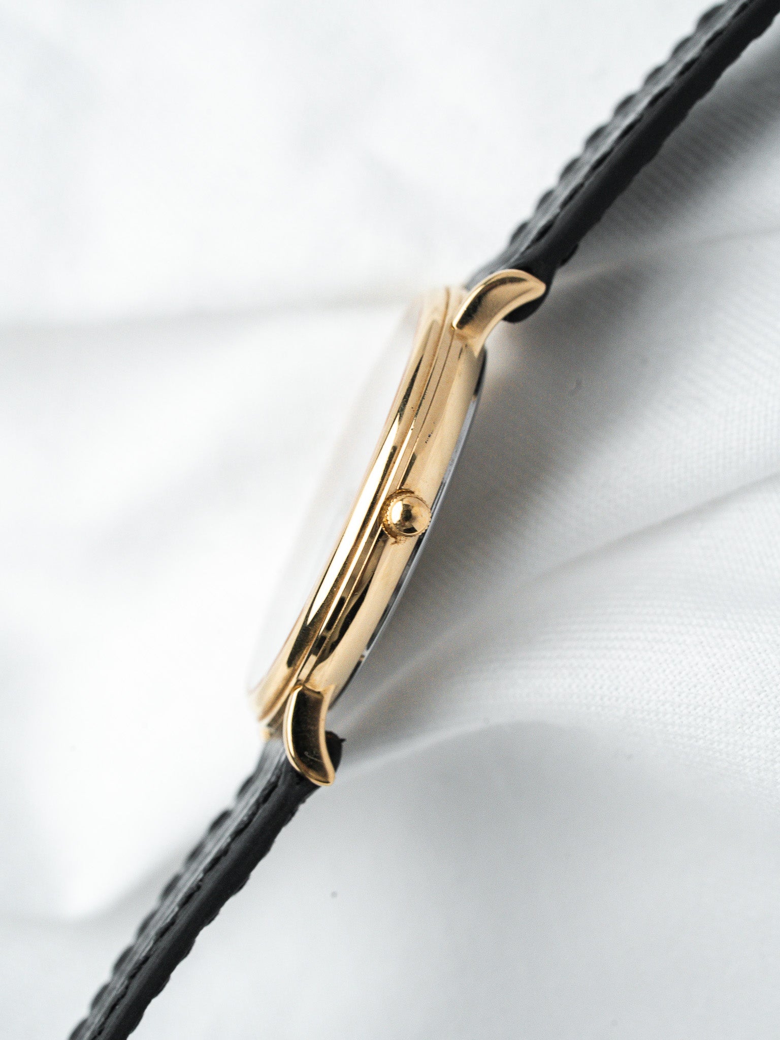 Vintage Cartier Tank watch with gold case and black leather strap on white fabric