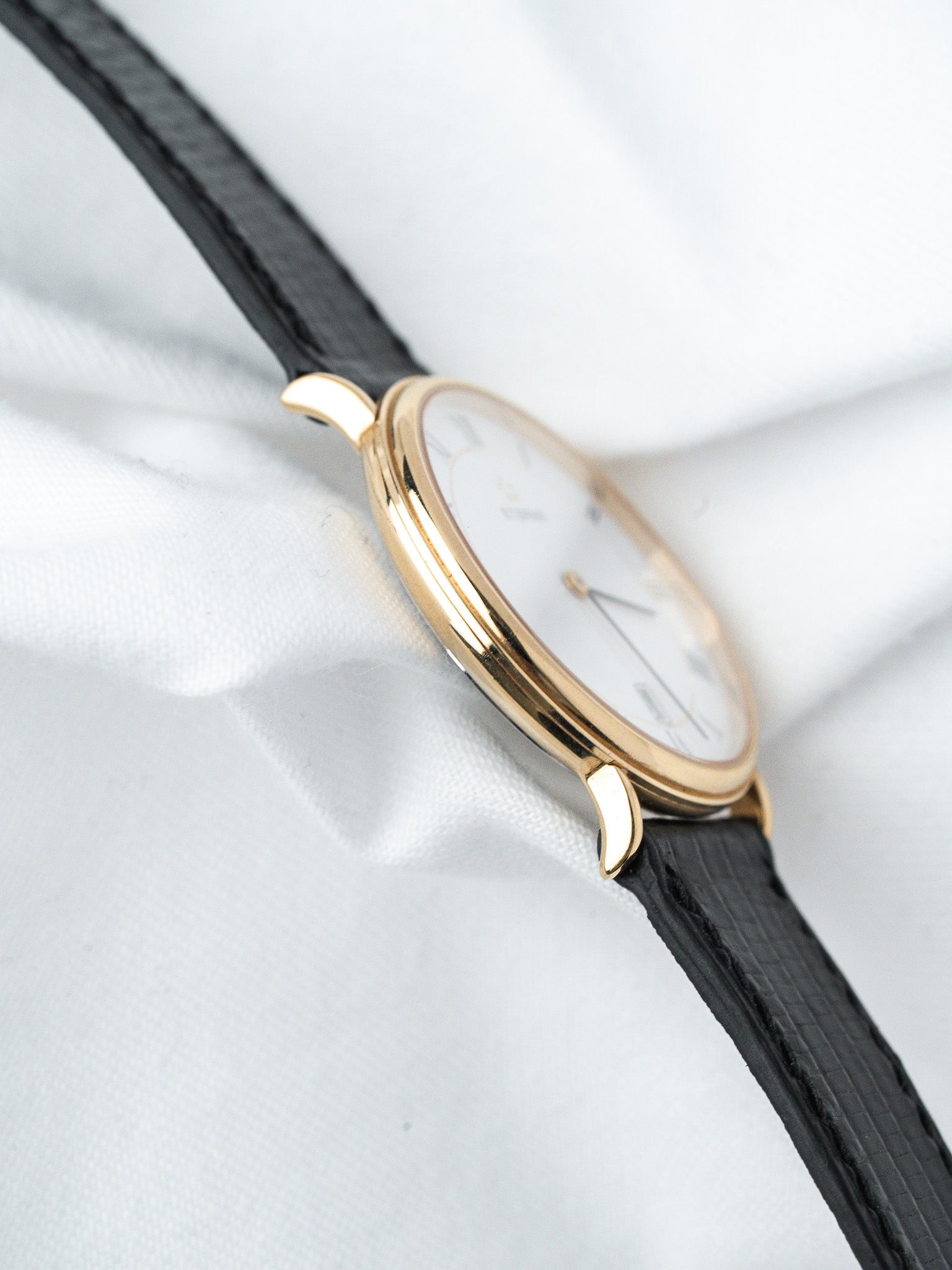 Vintage Universal Genève watch with gold case, white dial, black leather strap on white fabric
