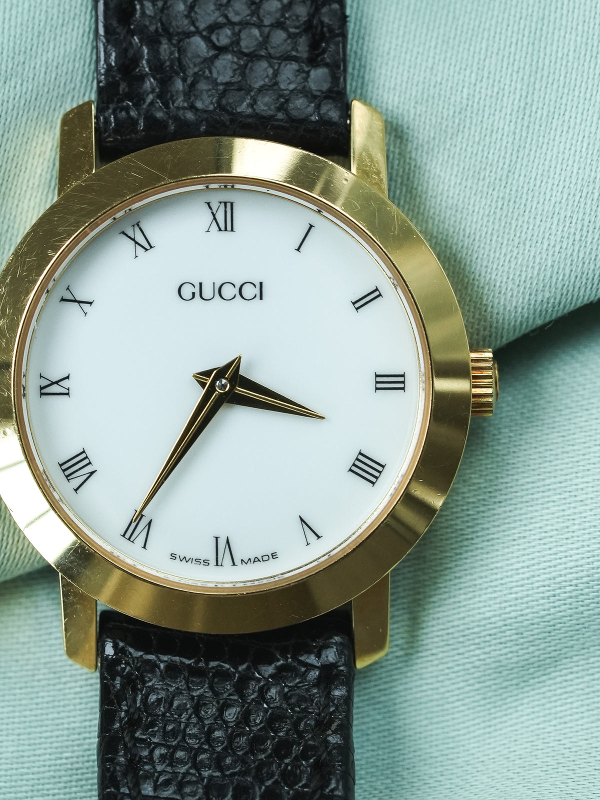 Gucci vintage watch with gold case, white dial, Roman numerals, black textured strap
