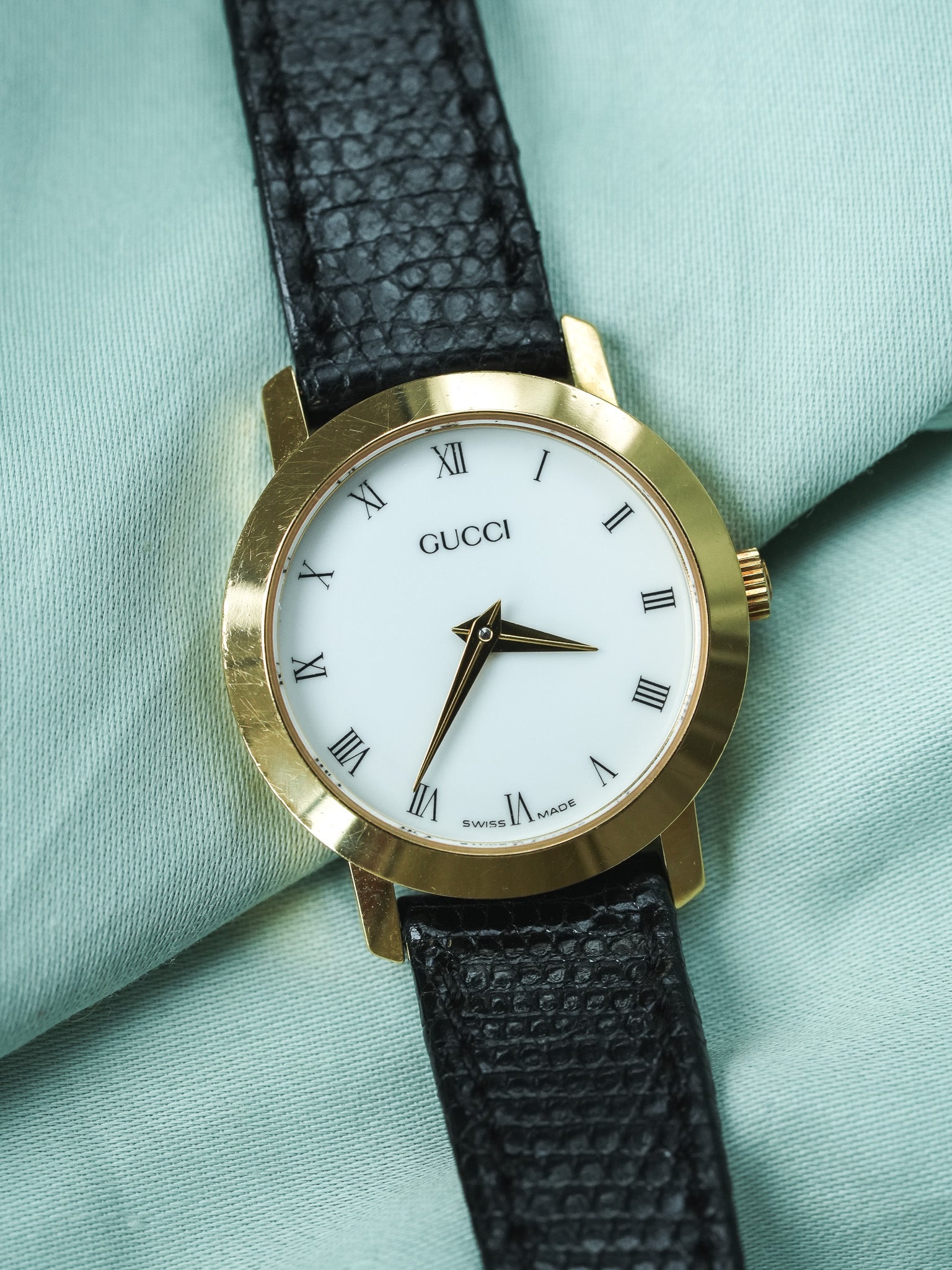Gucci vintage watch with gold case, white dial, Roman numerals, black textured strap
