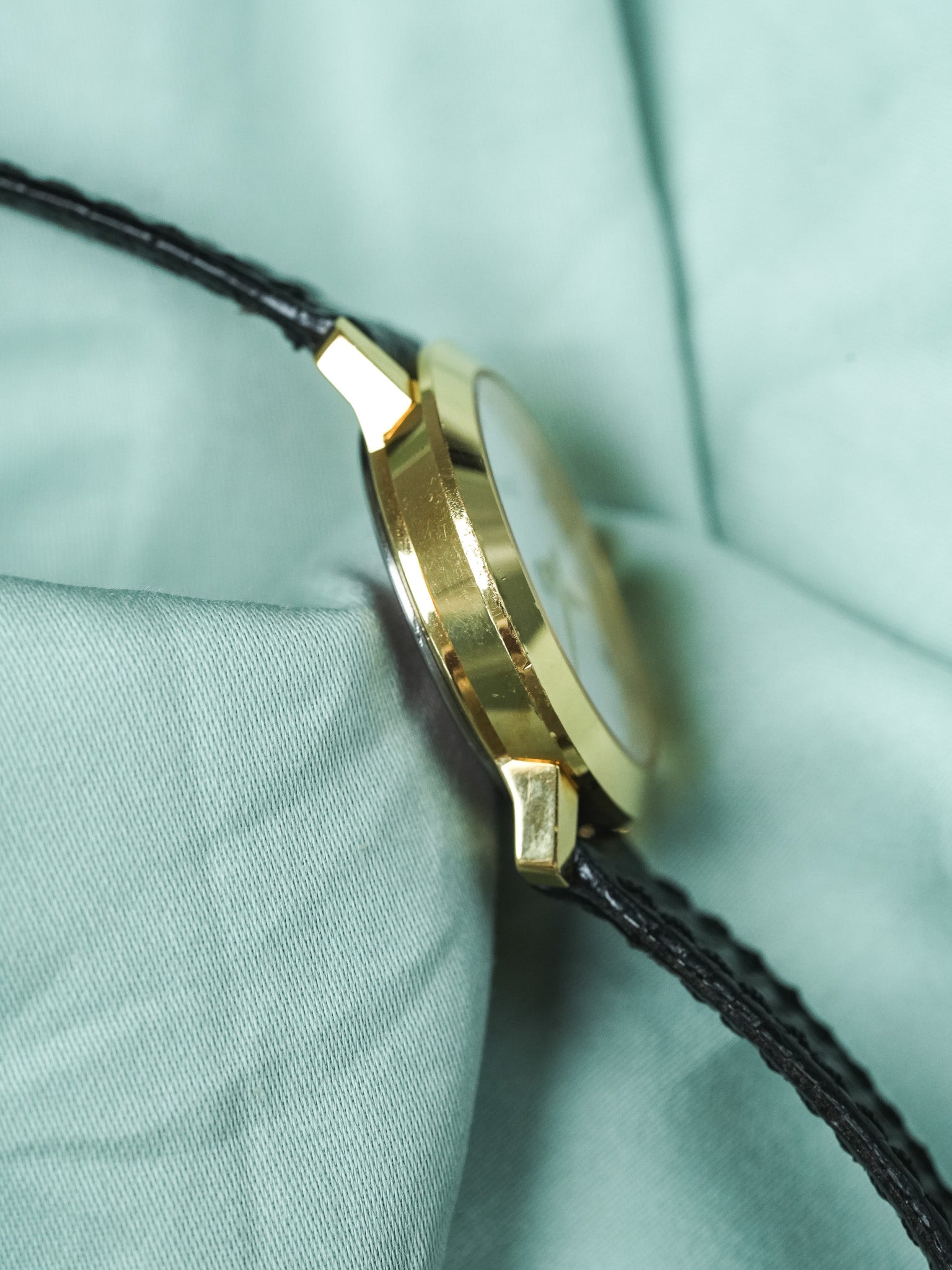 Vintage Cartier watch with gold case and black leather strap on mint fabric