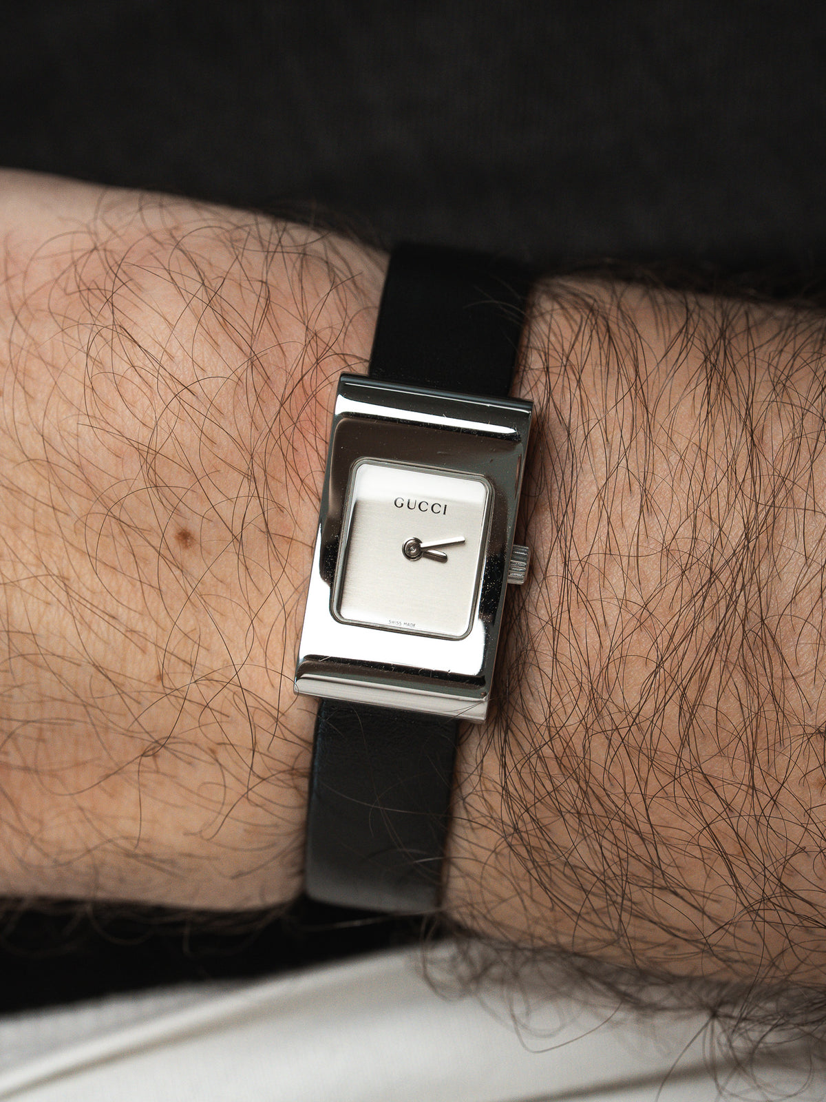 Gucci vintage watch with rectangular silver case, white dial, black leather strap on wrist