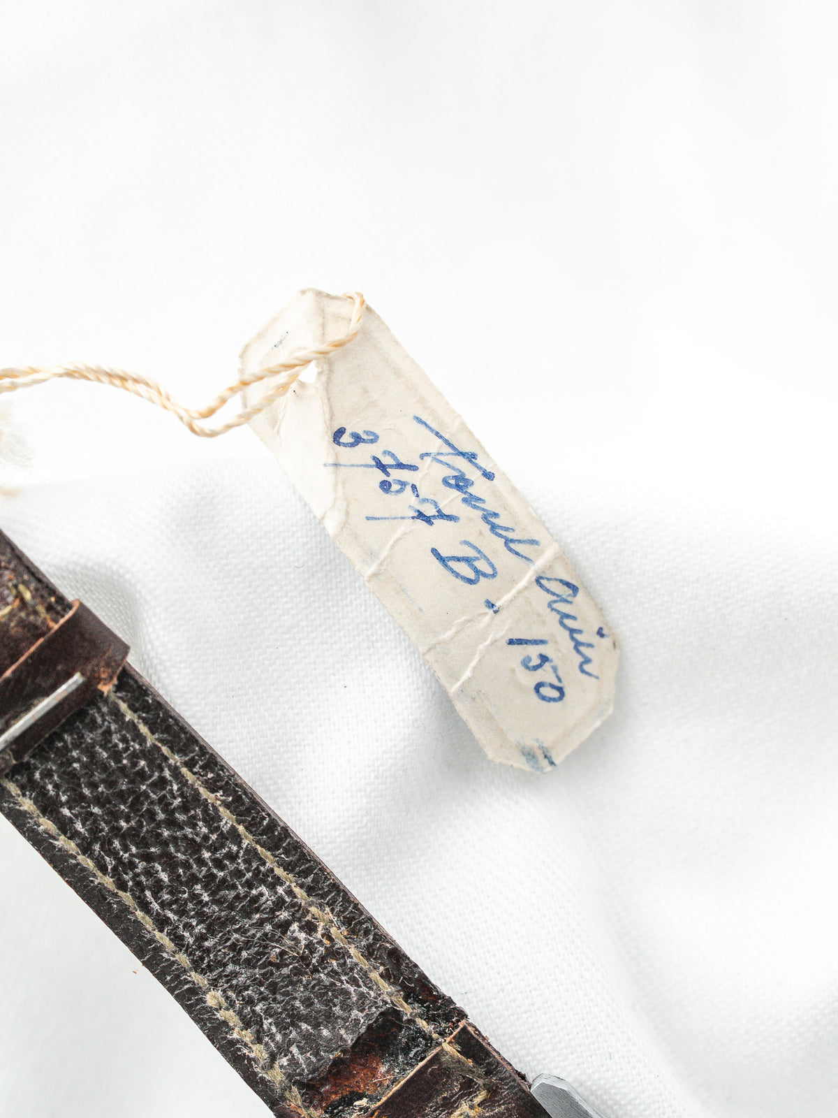 Étiquette d'inventaire vintage attachée à un bracelet en cuir noir sur fond blanc