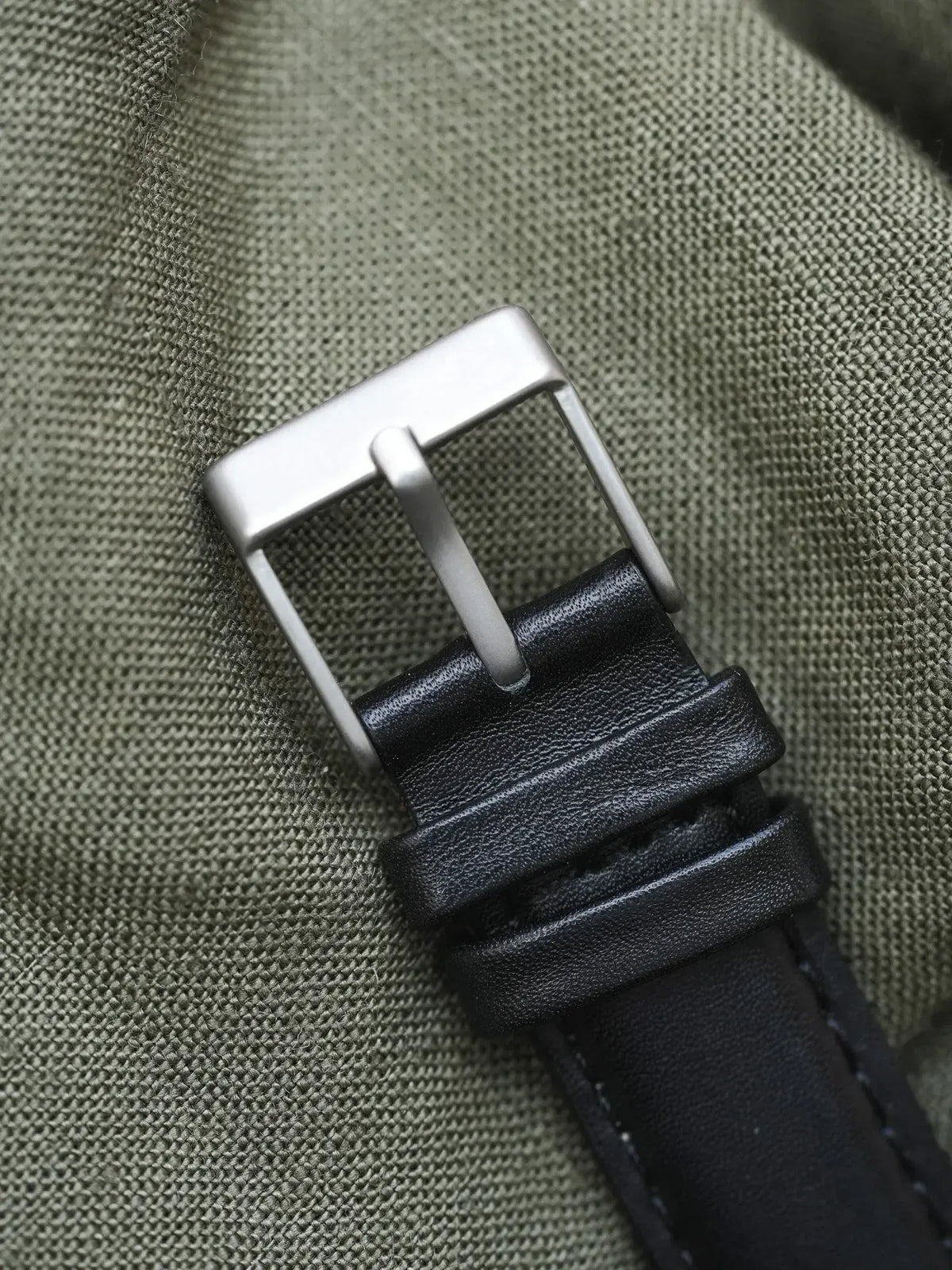 Black leather watch strap with brushed steel buckle on olive fabric