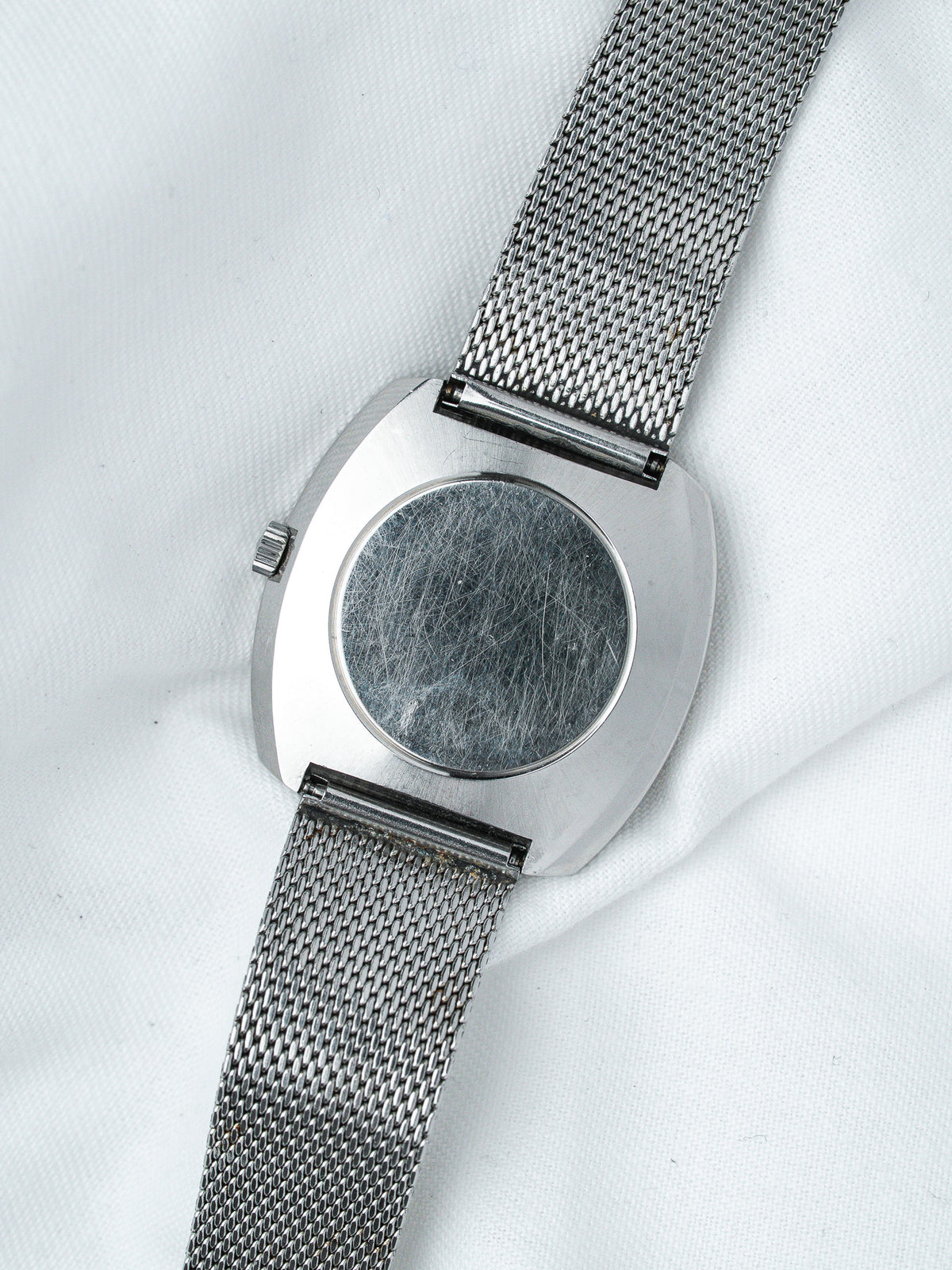 Vintage watch with mesh bracelet and scratched case back on white fabric