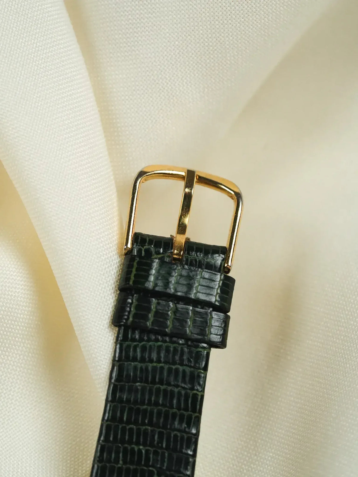 Vintage watch strap with green alligator texture and gold buckle on cream fabric