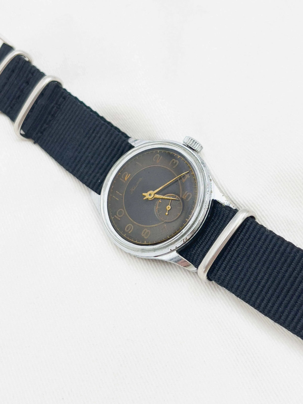 Vintage Universal Genève watch with dark dial, gold hands, steel case, black fabric strap
