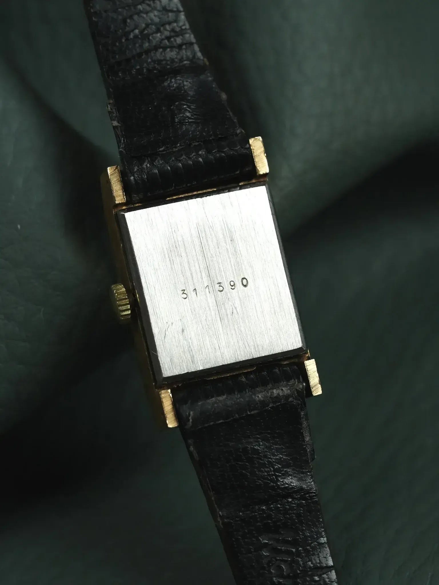 Vintage rectangular watch with gold case, black leather strap, and engraved case back number 311390