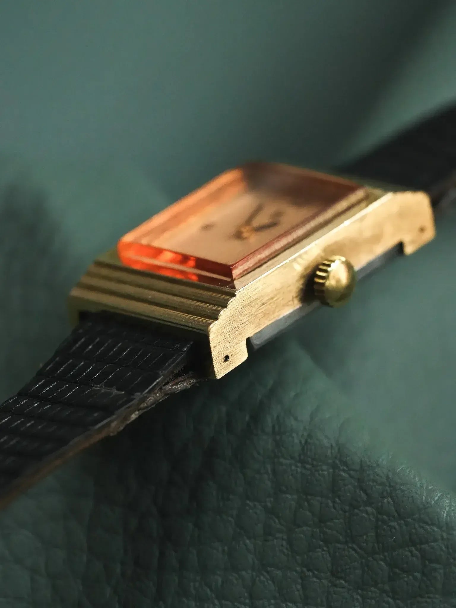 Vintage rectangular watch with gold case, amber crystal, black textured strap on green leather