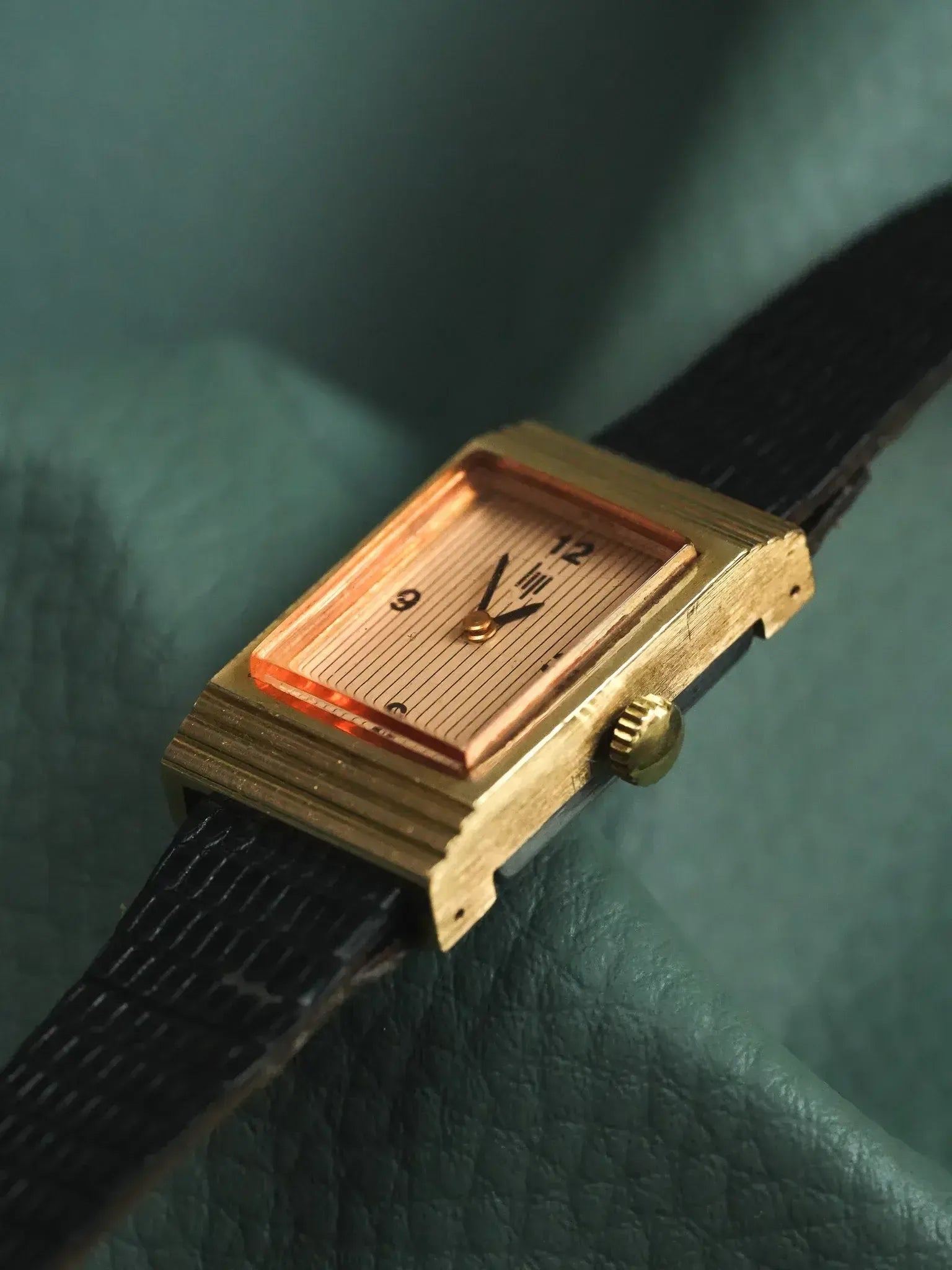 Vintage rectangular gold watch with striped dial, black leather strap on green leather