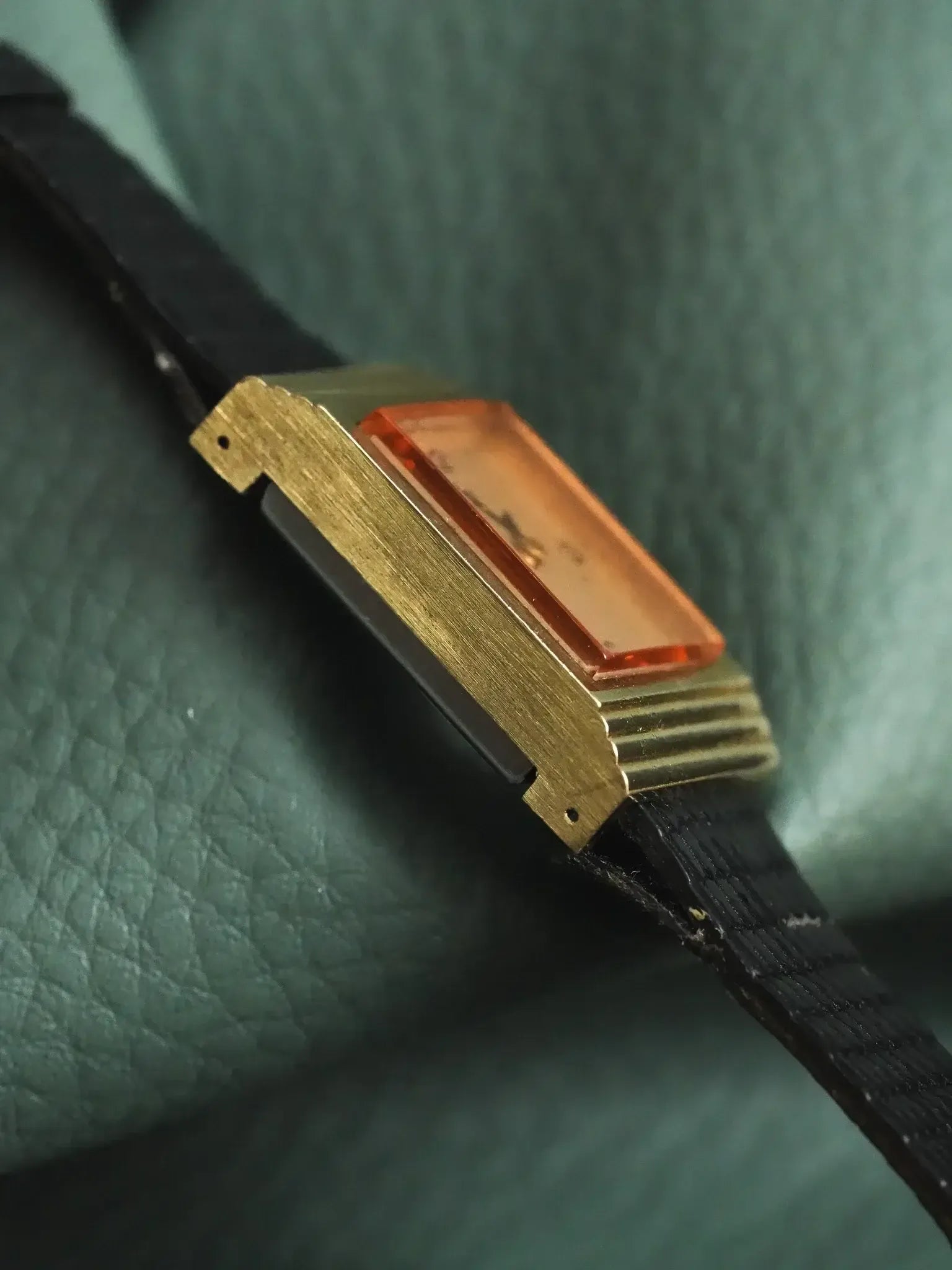 Vintage Cartier watch with gold case, amber crystal, black leather strap on green texture