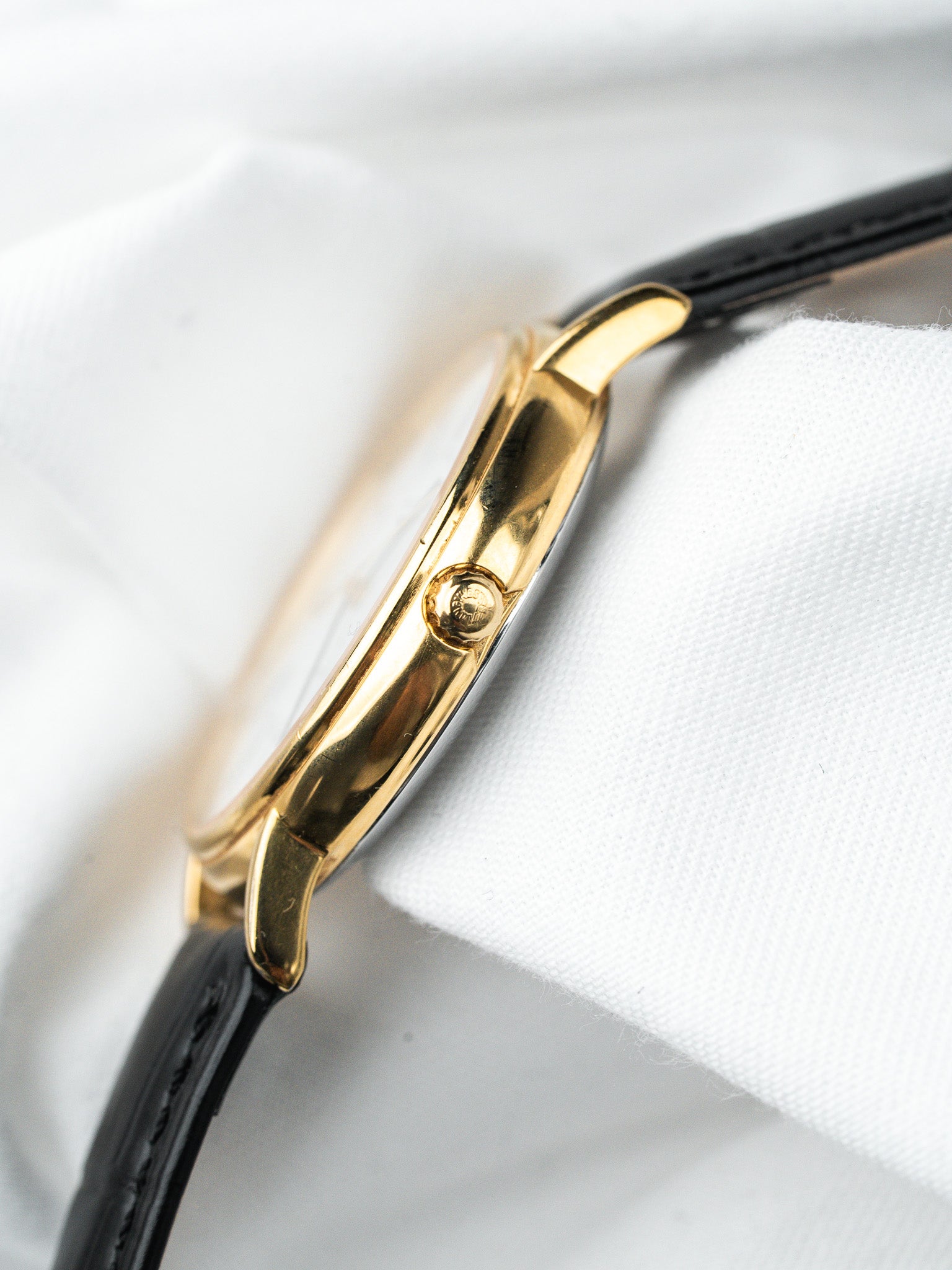Vintage Cartier watch with gold case and black leather strap on white fabric
