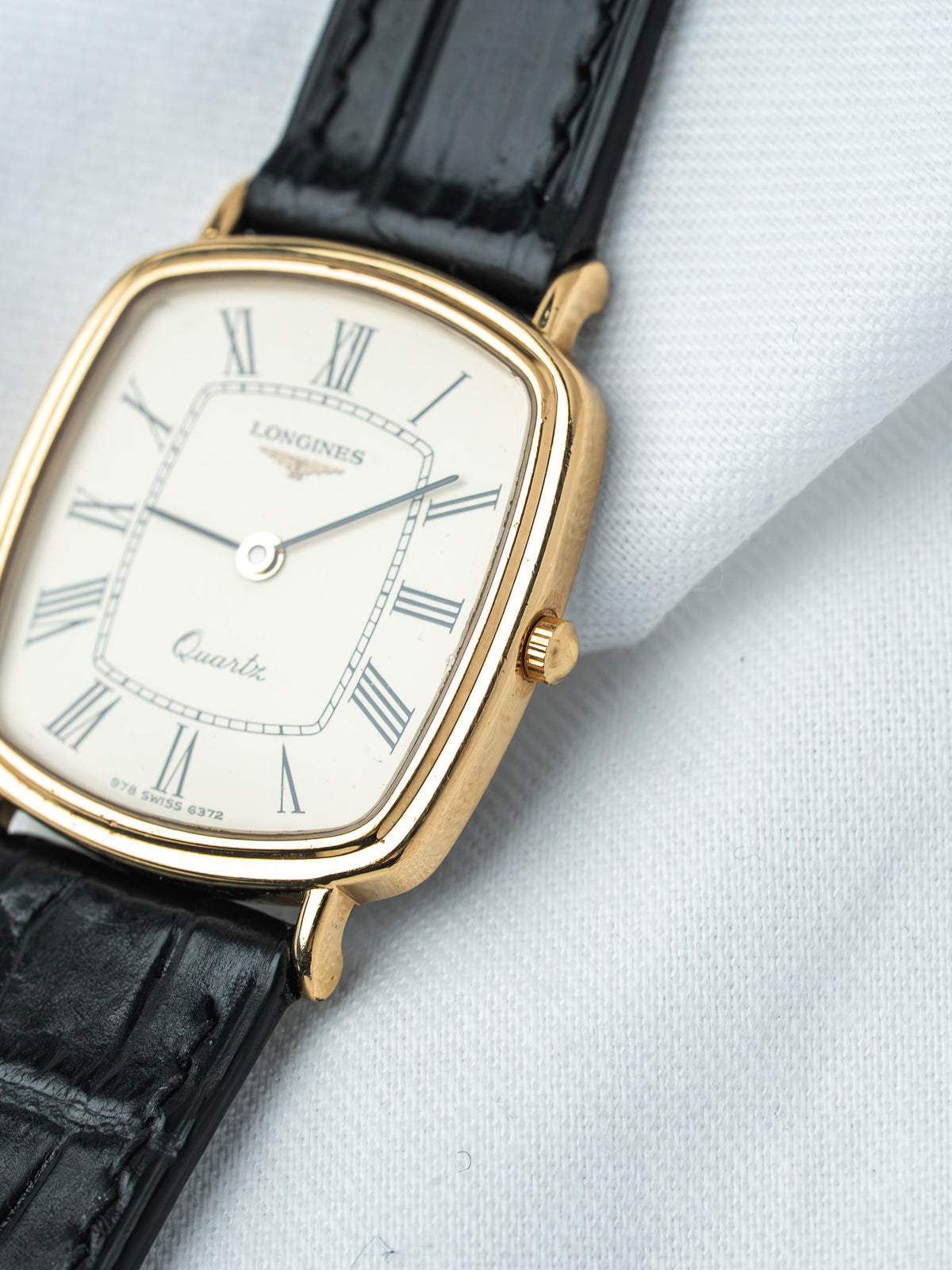Longines vintage quartz watch with gold case, white dial, Roman numerals, black leather strap