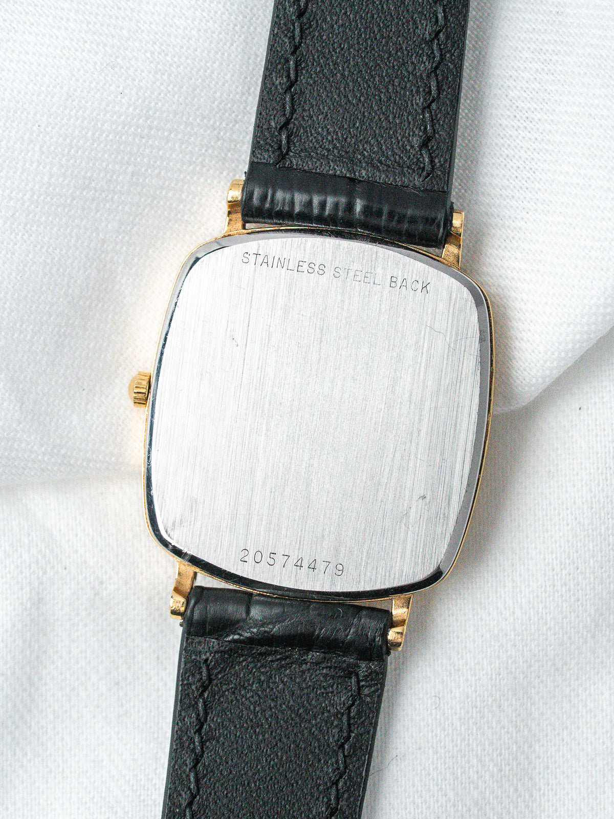 Vintage watch with gold case, stainless steel back, black leather strap on white fabric