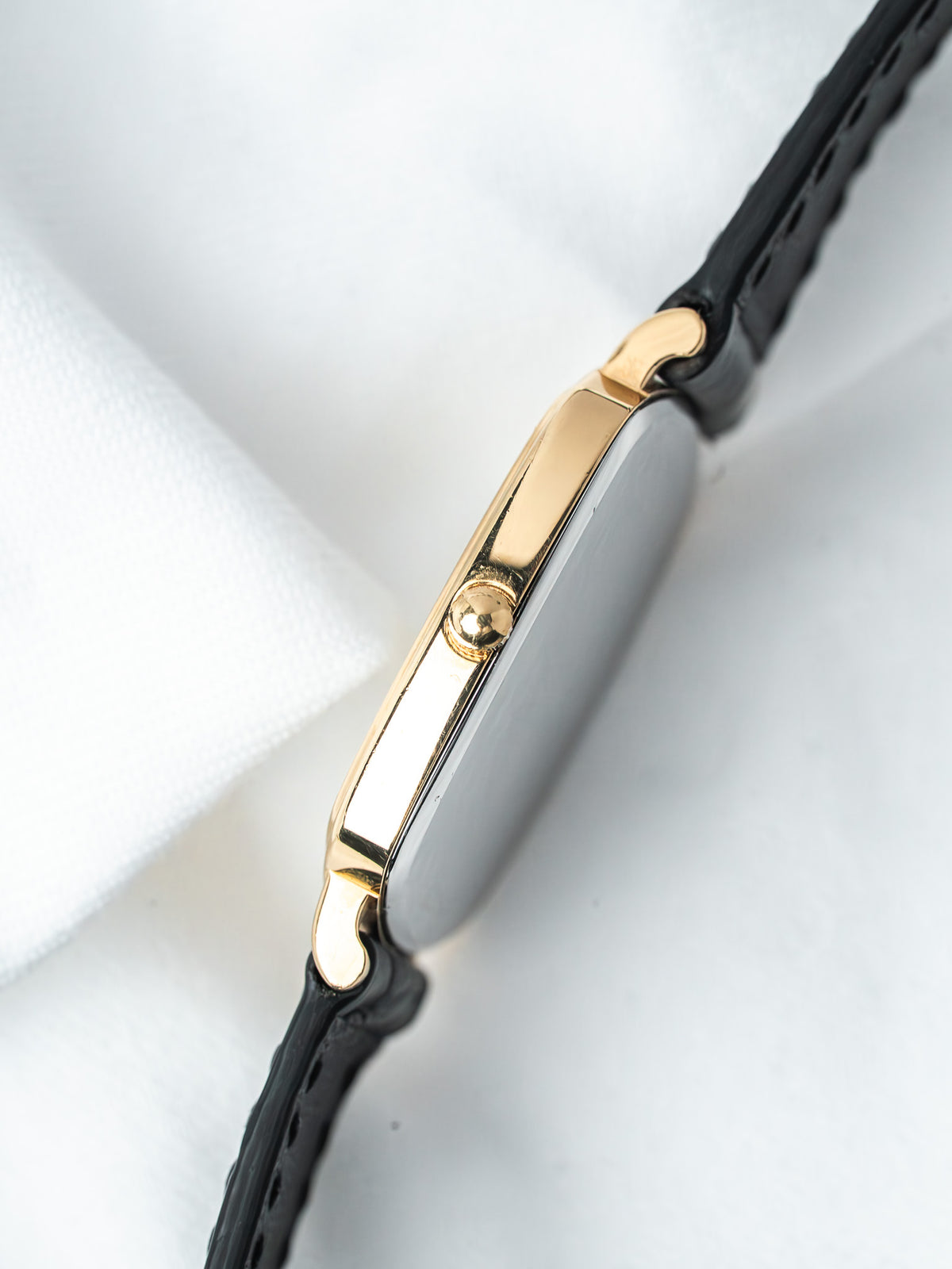 Cartier Tank vintage watch with gold case and black leather strap on white background