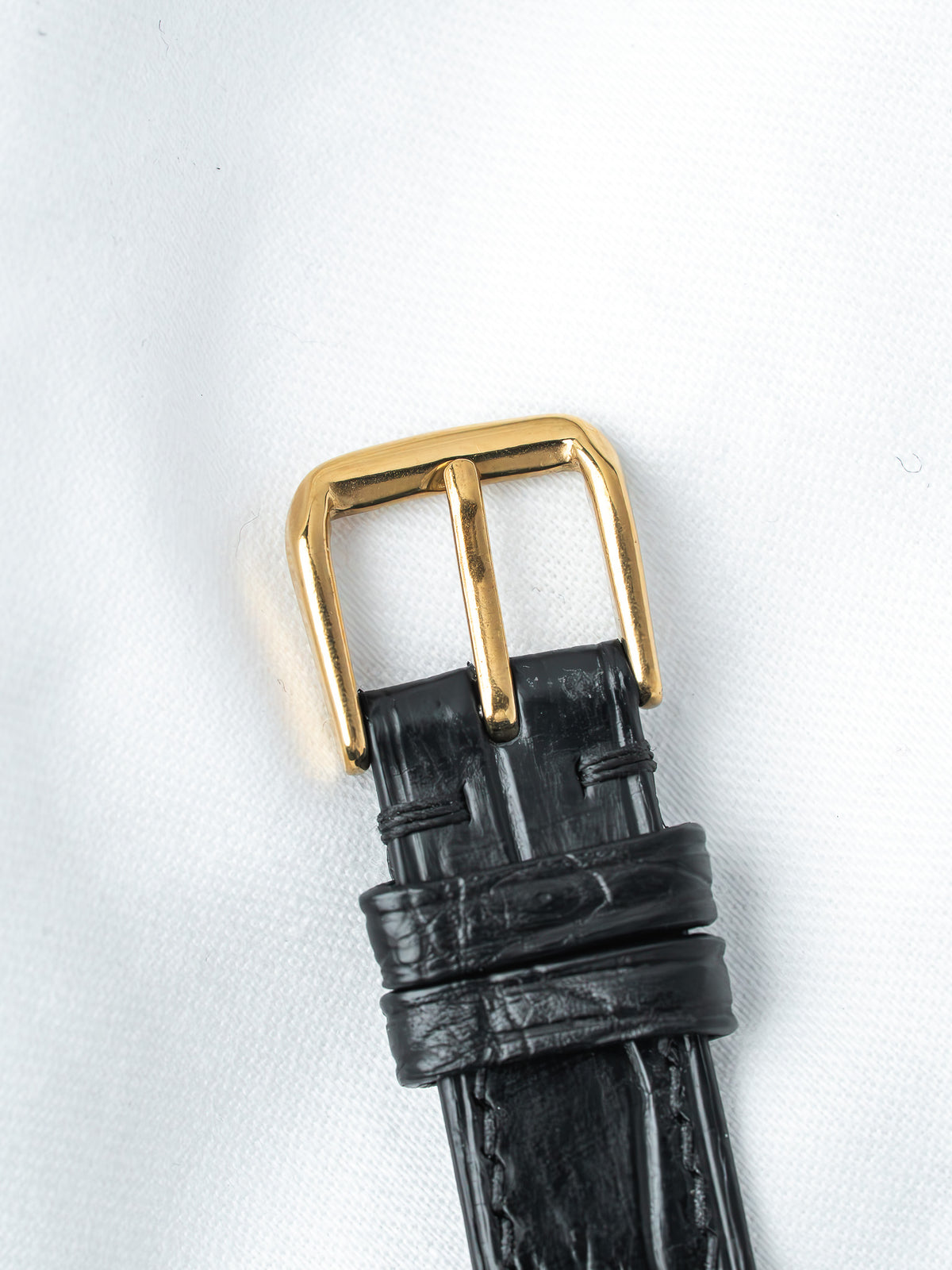 Black alligator leather watch strap with gold buckle on white background