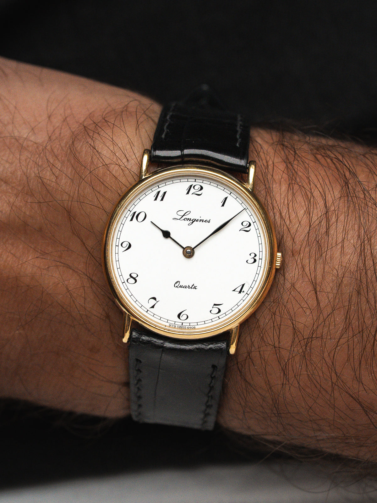 Montre Longines vintage avec cadran blanc, boîtier doré et bracelet en cuir noir.