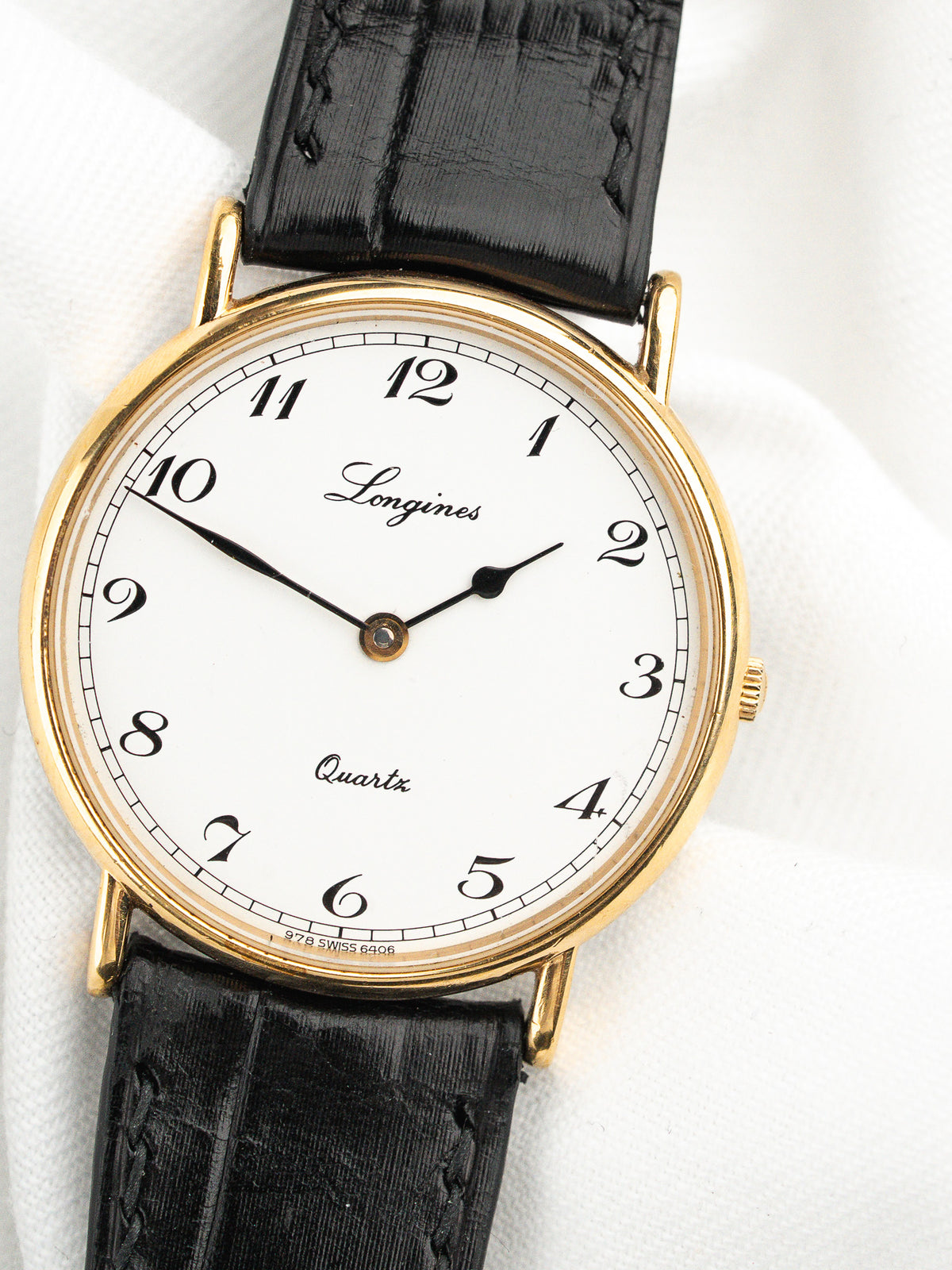 Montre Longines vintage avec cadran blanc, boîtier doré et bracelet en cuir noir.
