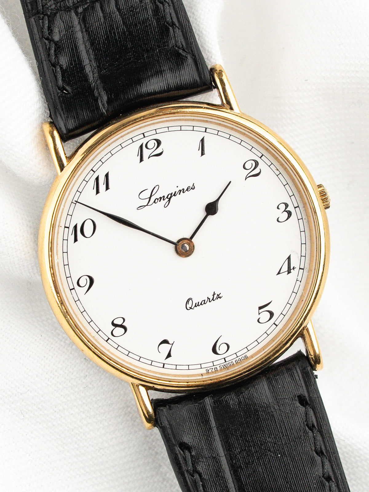 Montre Longines vintage au cadran blanc, boîtier doré et bracelet en cuir noir.