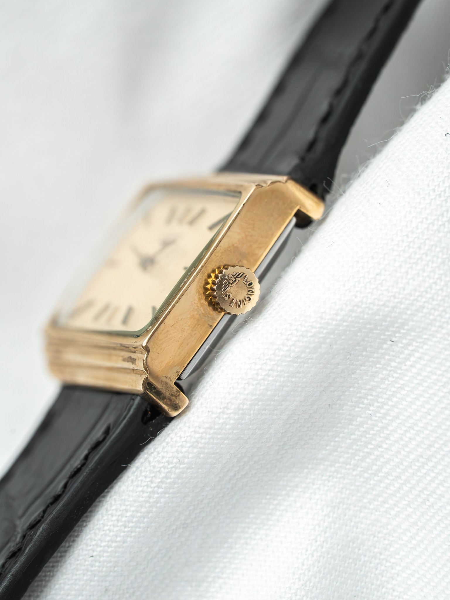 Longines vintage watch with gold case, cream dial, black leather strap on white fabric