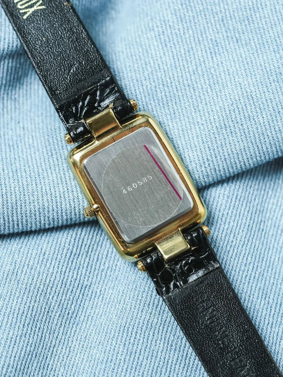 Vintage Cartier watch with gold case, black alligator strap, on denim background