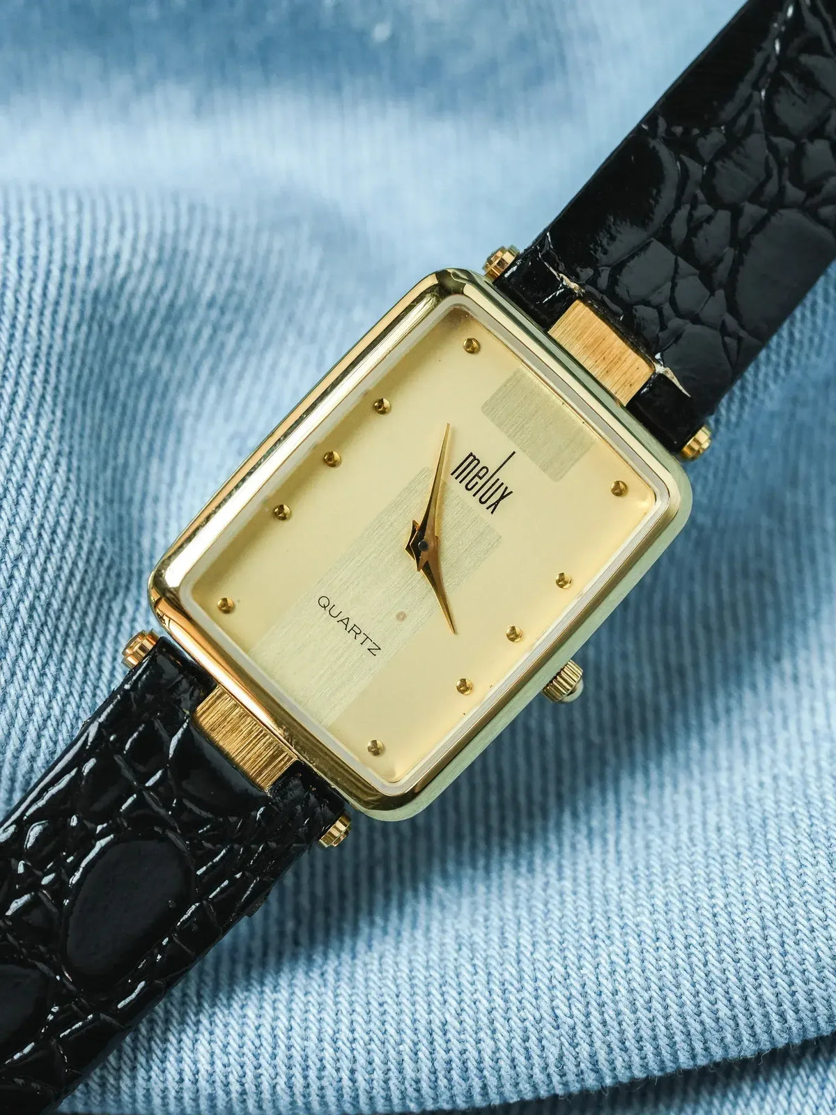 Melux vintage quartz watch with gold case, cream dial, black crocodile strap on denim