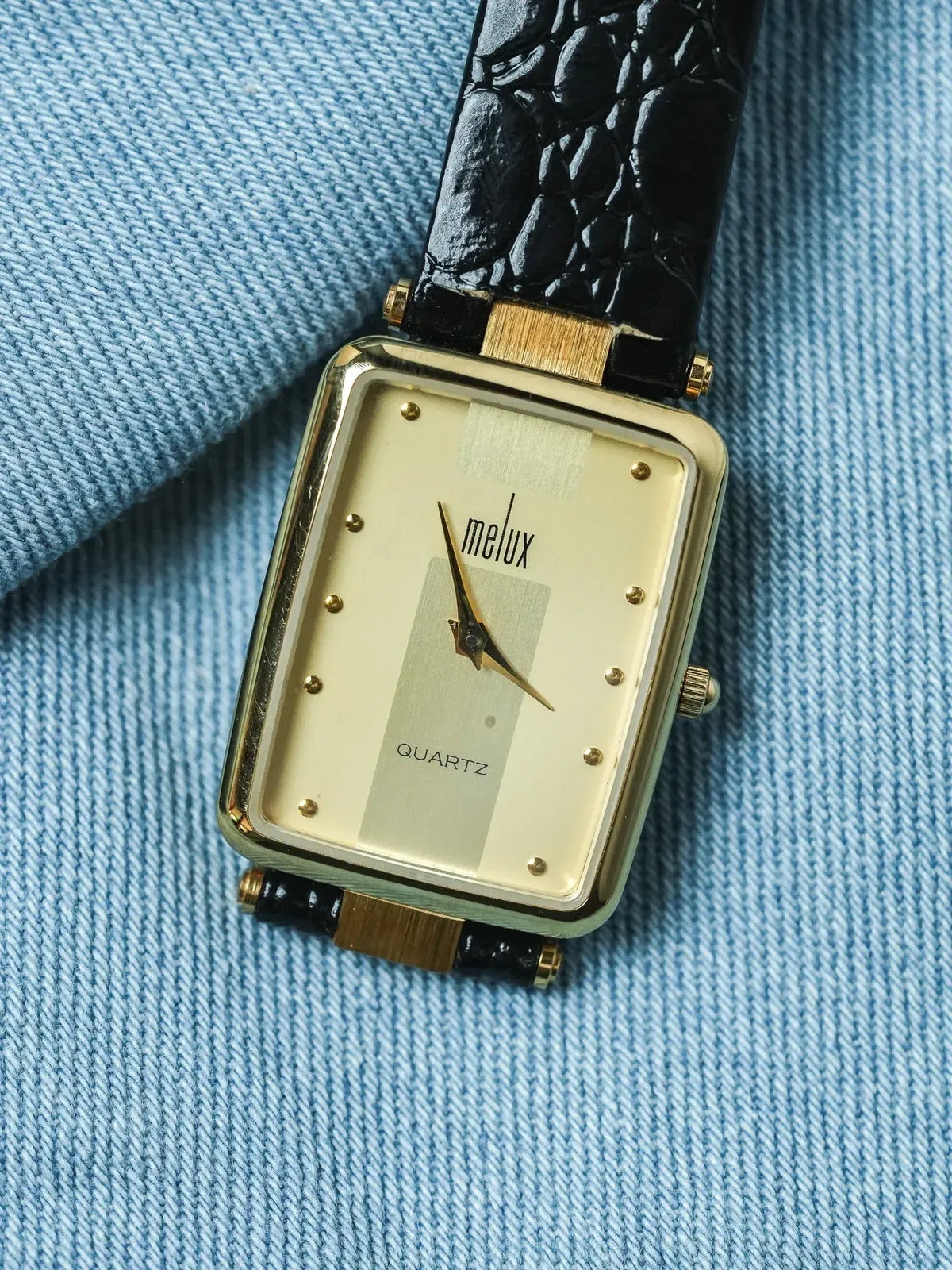 Melux vintage quartz watch with gold case, cream dial, black leather strap on denim