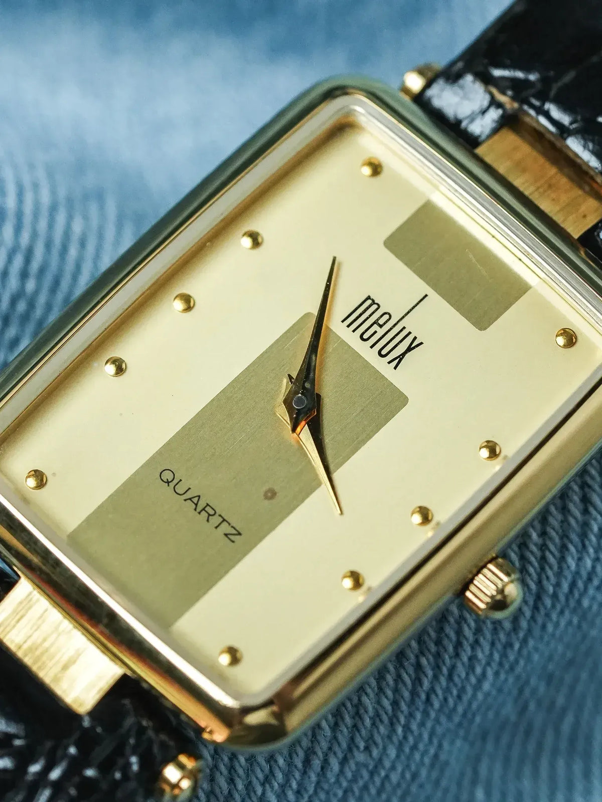 Melux vintage quartz watch with gold case, cream dial, black leather strap on denim