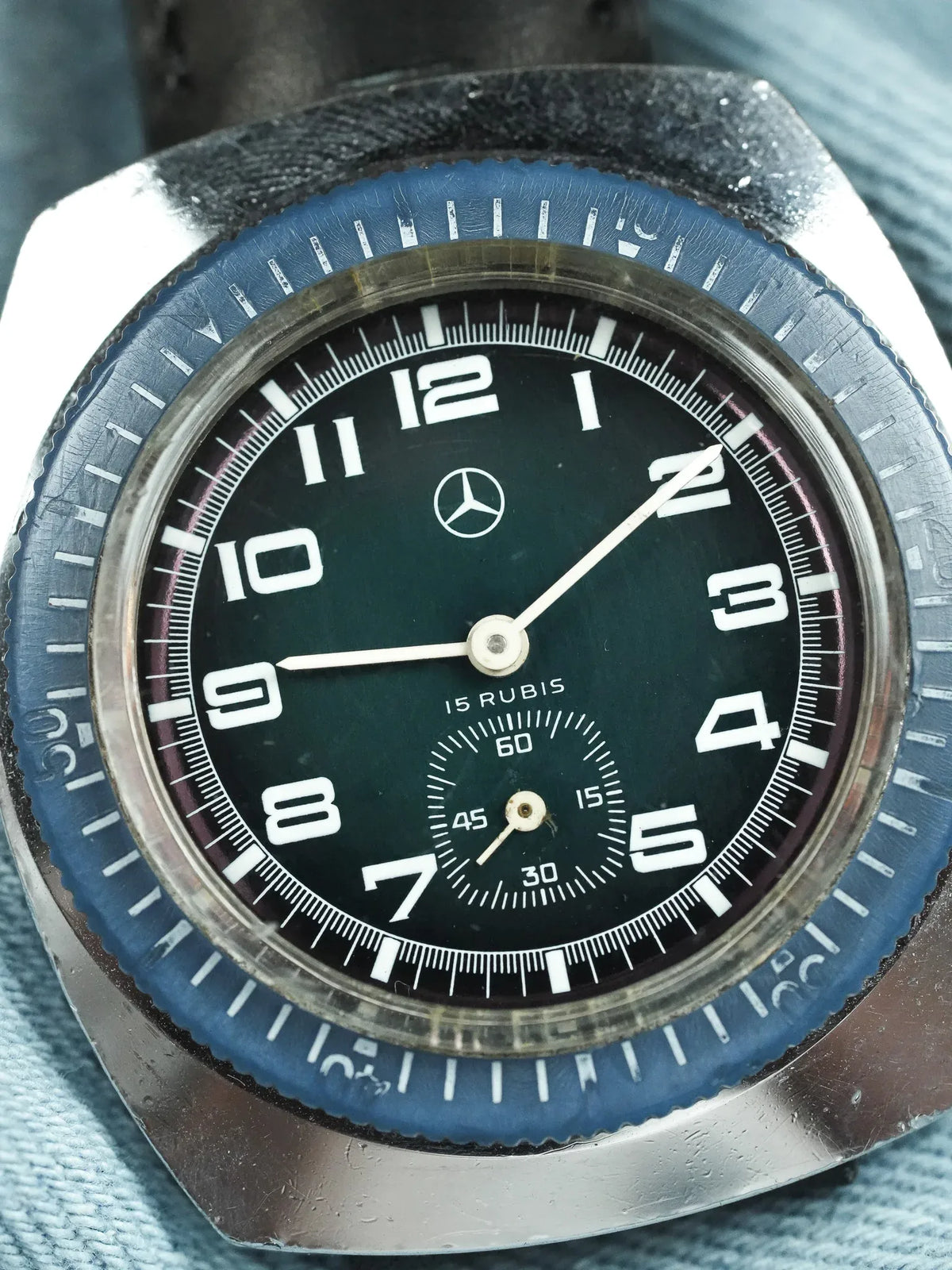 Vintage Mercedes-Benz watch with black dial, white numerals, blue bezel, and steel case