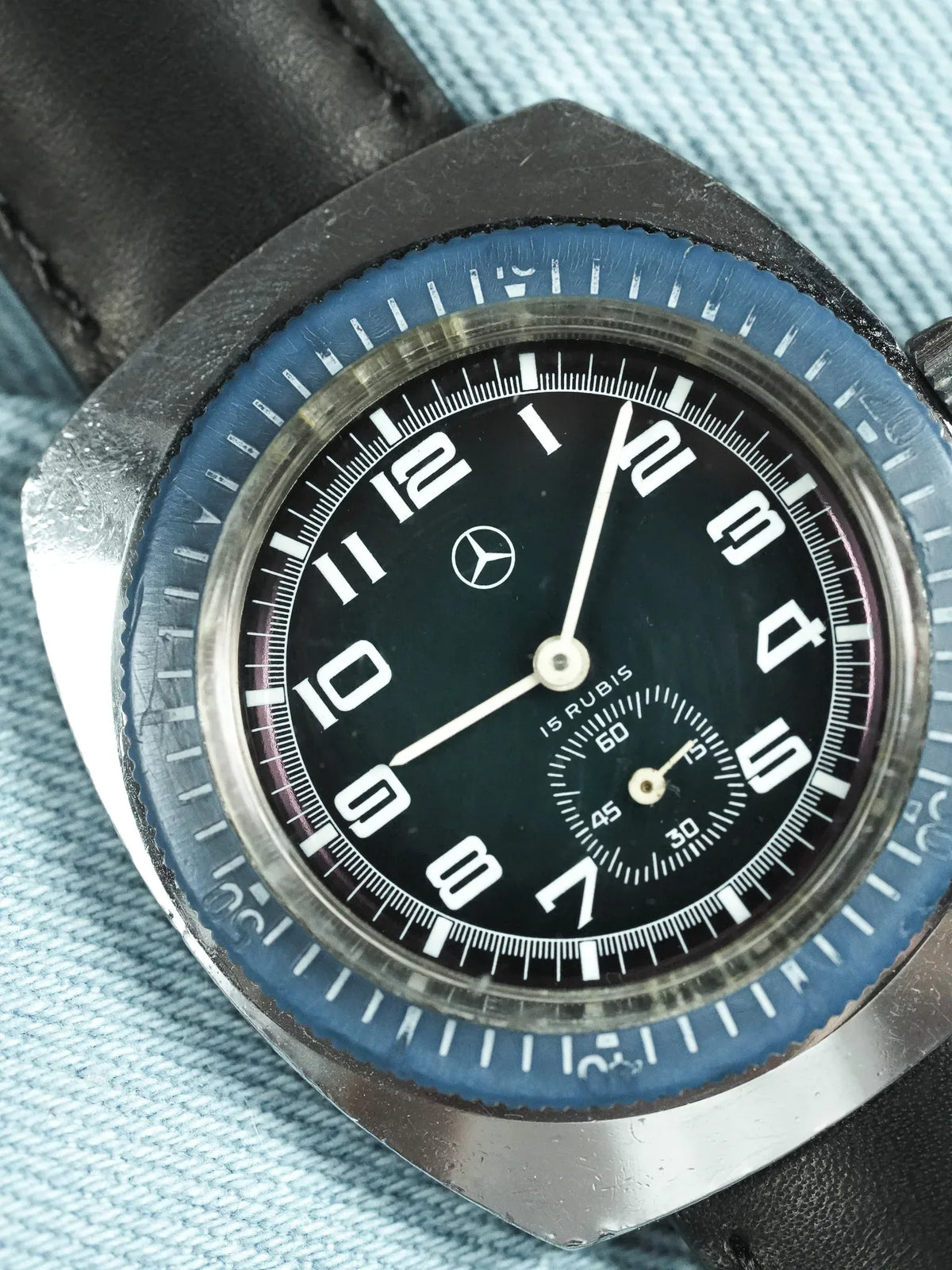 Vintage Mercedes-Benz watch with black dial, blue bezel, and leather strap on denim
