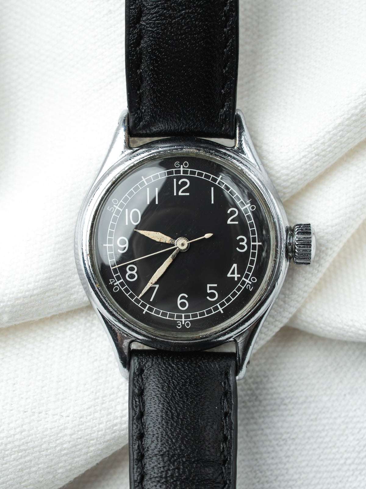 Vintage watch with black dial, white numerals, steel case, black leather strap on white fabric