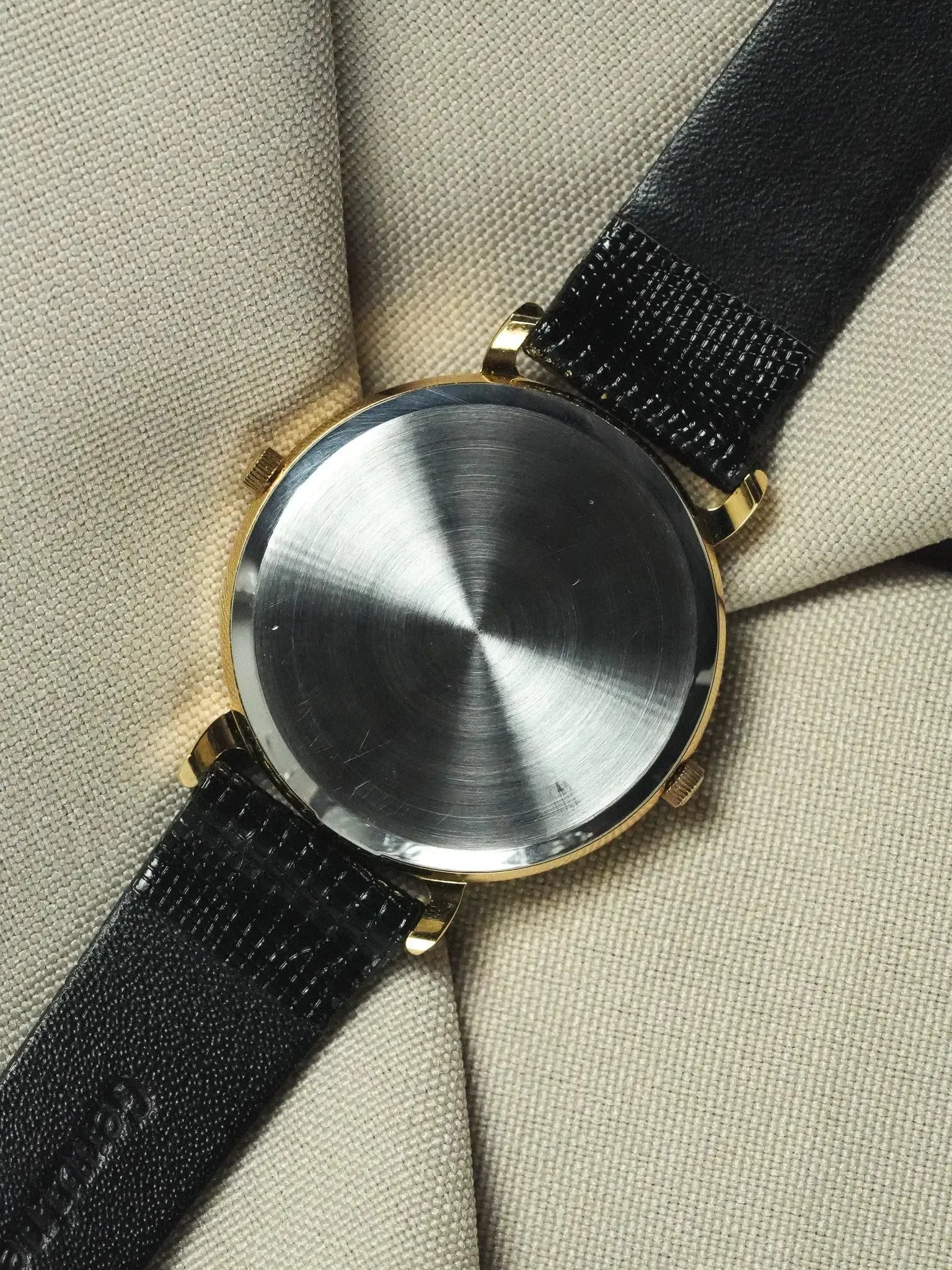 Vintage watch with gold case, brushed steel back, black textured strap on fabric