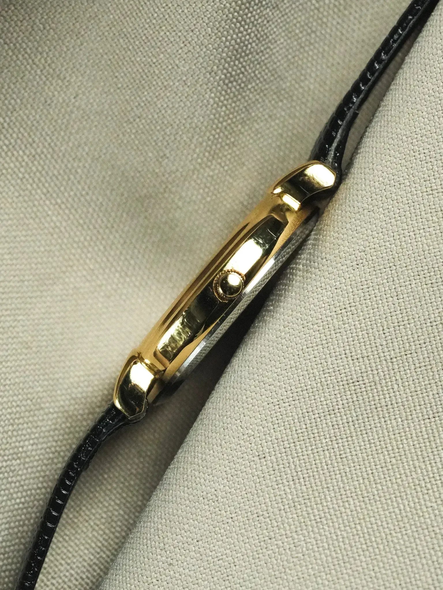Vintage Cartier Tank watch with gold case and black leather strap on textured fabric