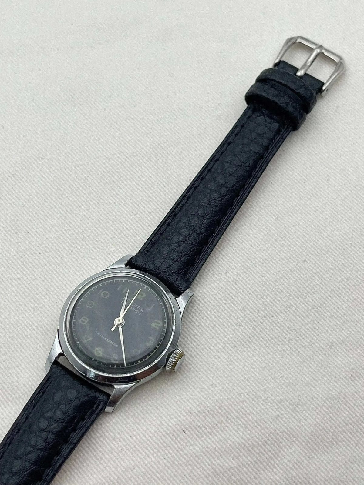Vintage Moscow watch with grey dial, black leather strap, and steel case on textured background