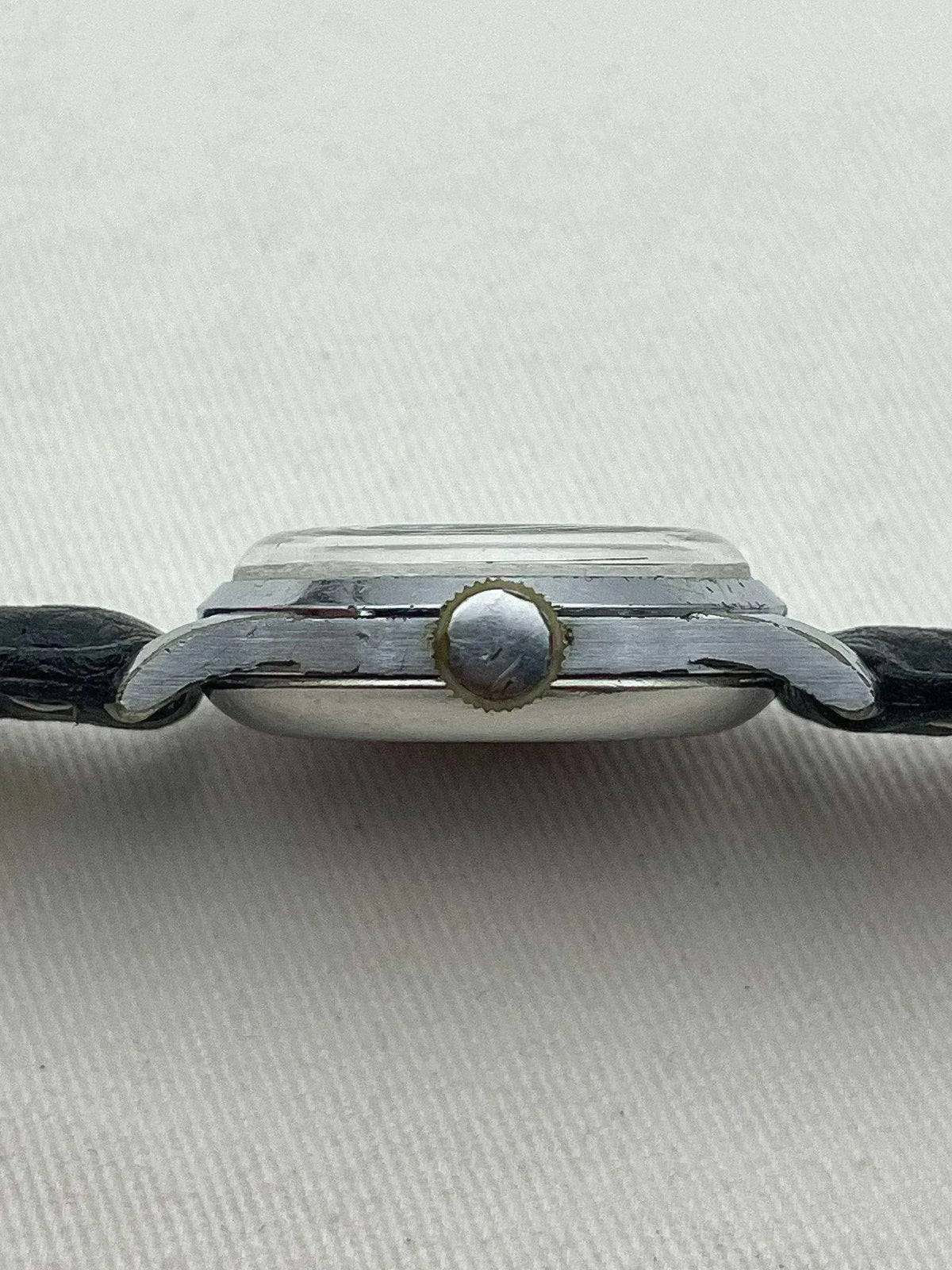 Vintage watch with silver case, black leather strap, and textured crown on white background