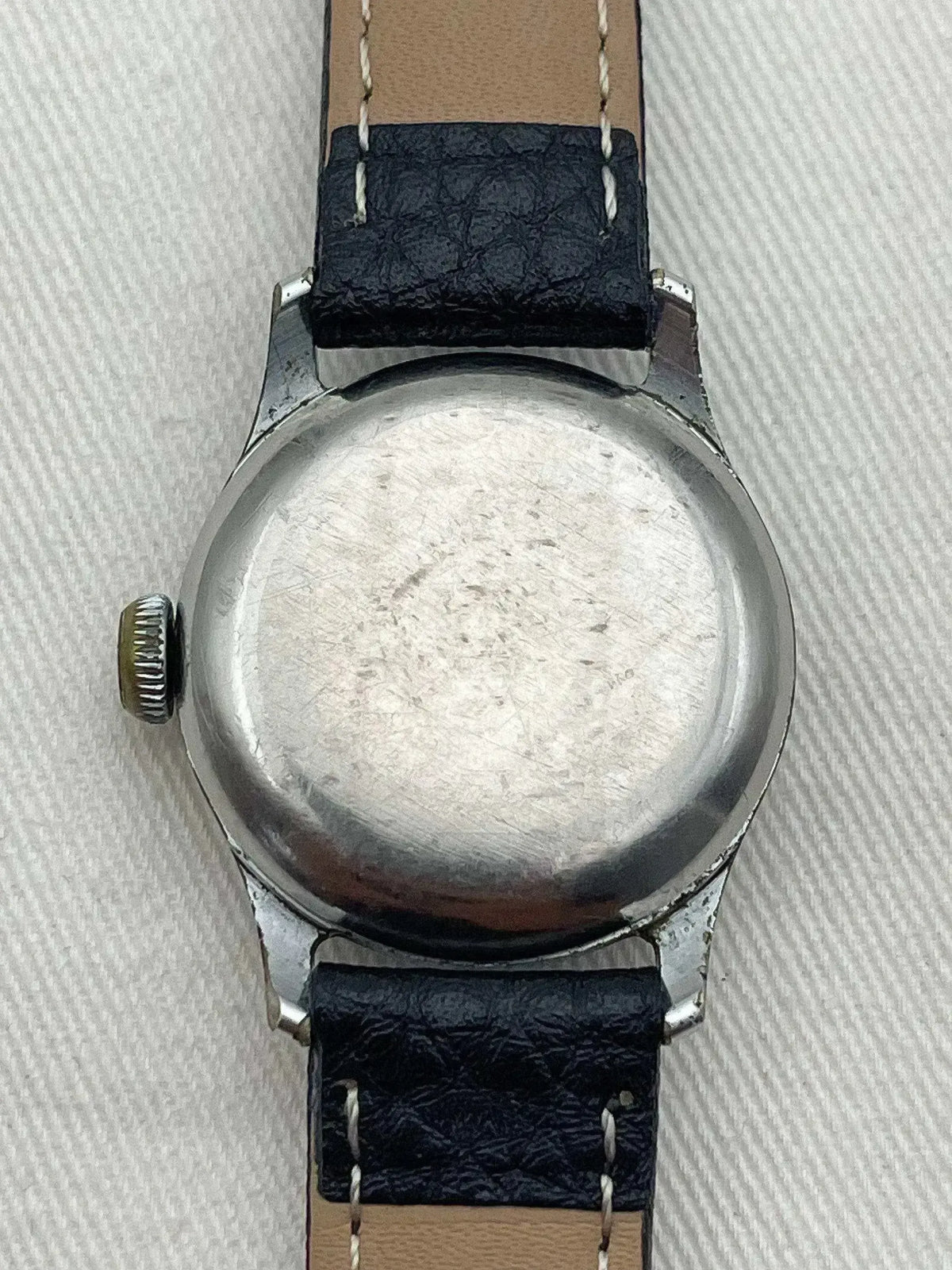 Vintage watch back with brushed steel case, black leather strap, visible crown on textured surface