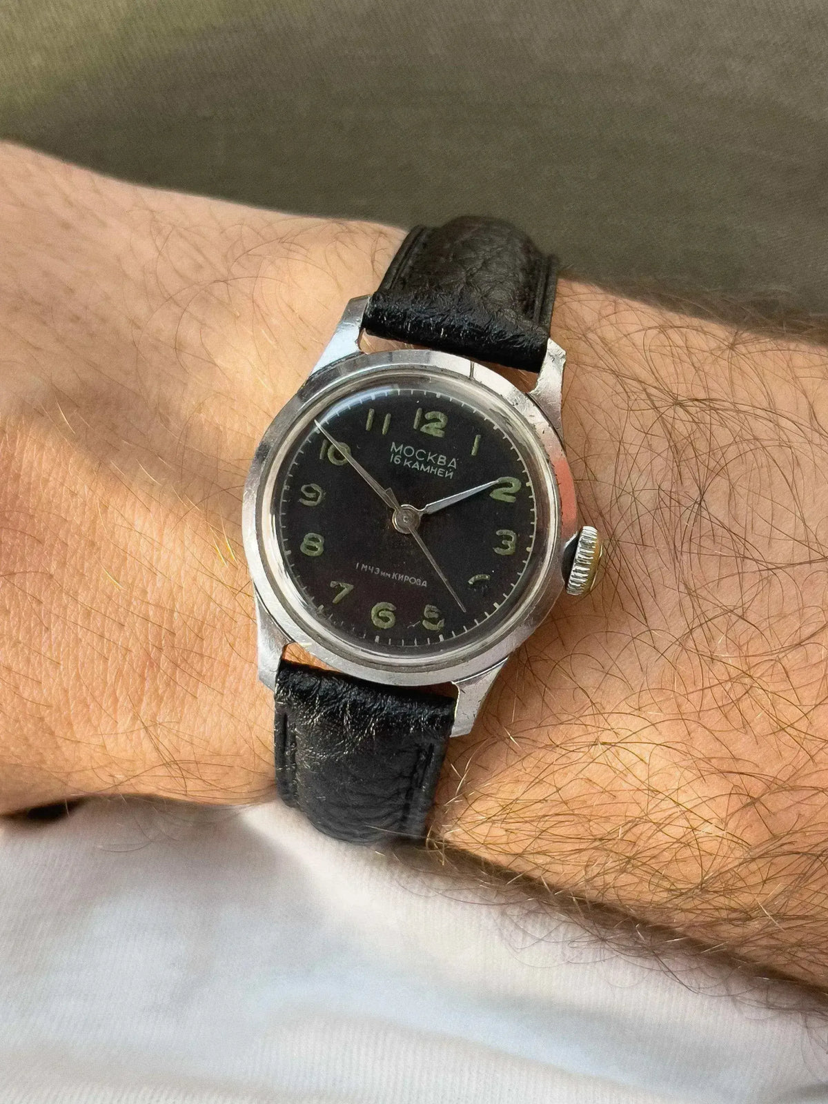 Vintage Moscow watch with black dial, luminous numerals, steel case, and black leather strap on wrist