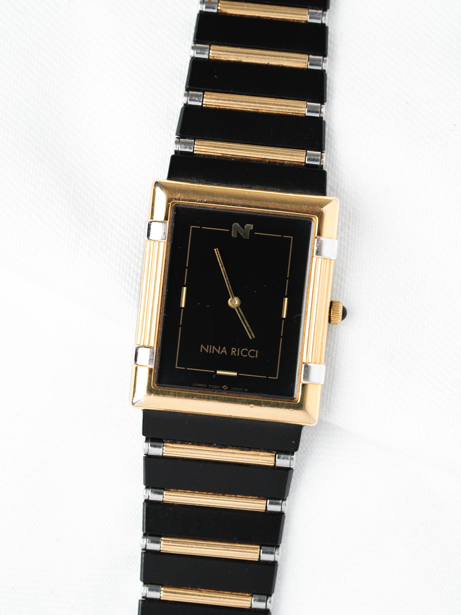 Nina Ricci vintage watch with black dial, gold case, and two-tone bracelet on white background