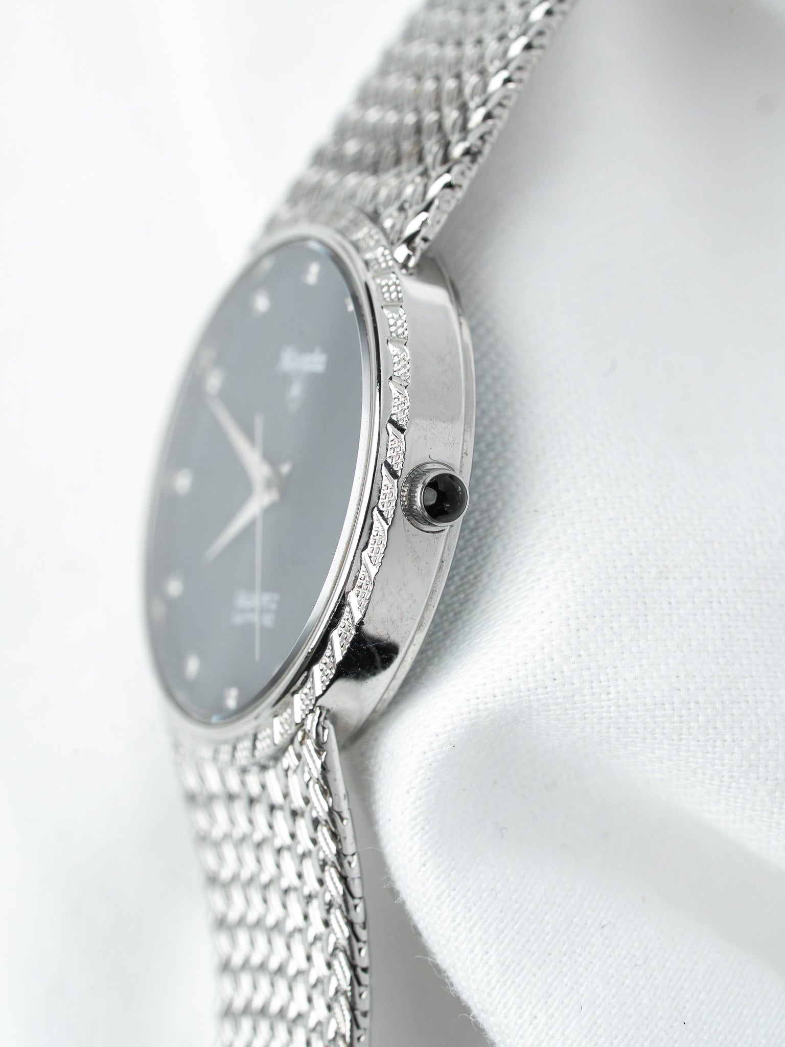 Vintage Omega watch with gray dial, textured bezel, and mesh bracelet on white fabric