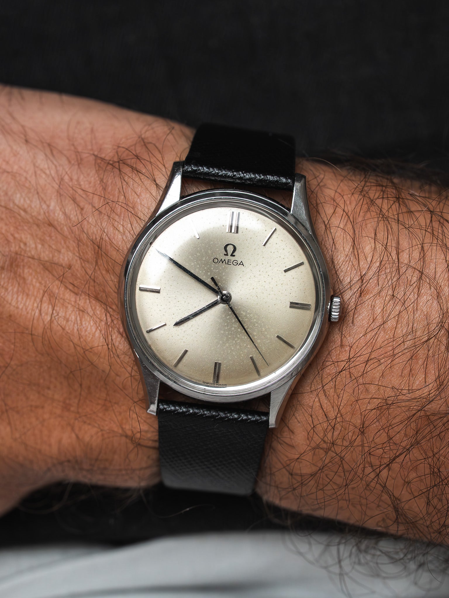 Vintage Omega watch with cream dial, black leather strap, worn on wrist