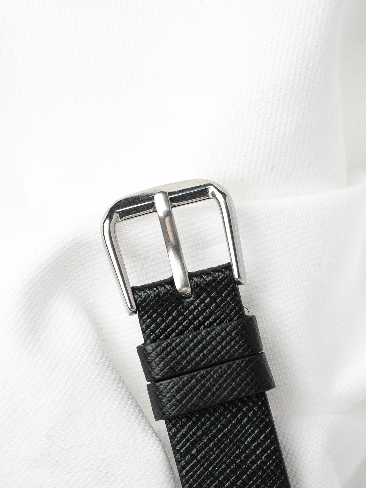 Black textured leather watch strap with polished silver buckle on white fabric