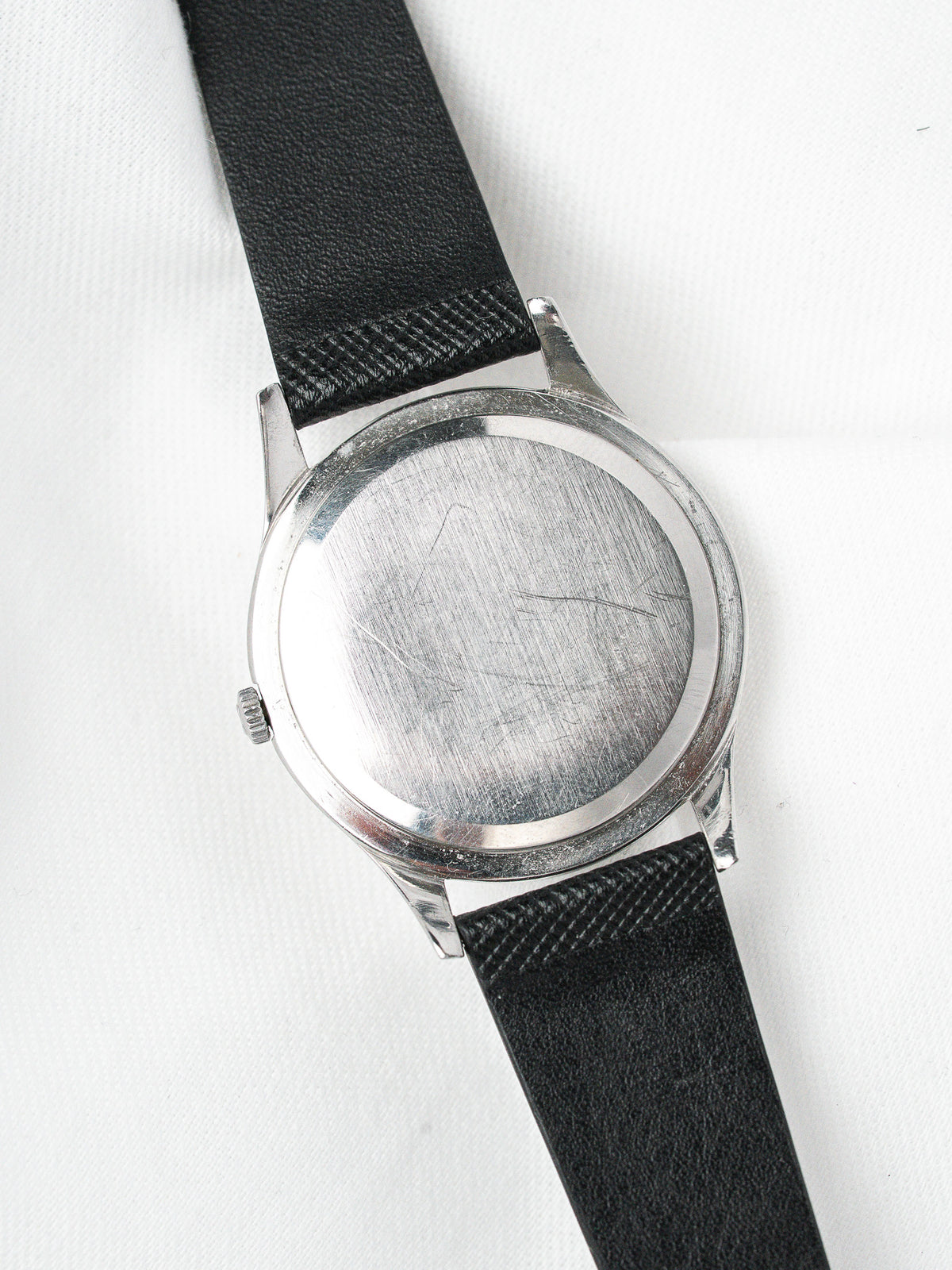 Vintage watch with brushed steel case and black leather strap on white background