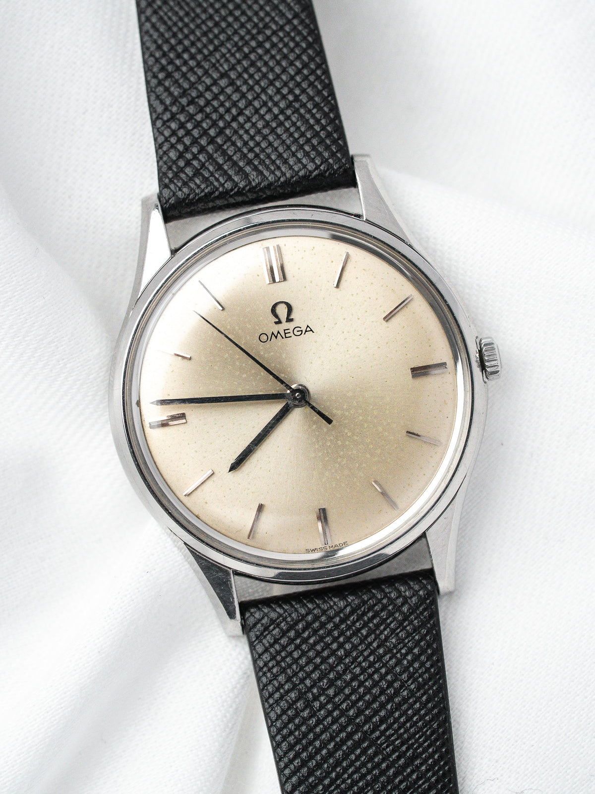 Vintage Omega watch with cream dial, black strap, and stainless steel case