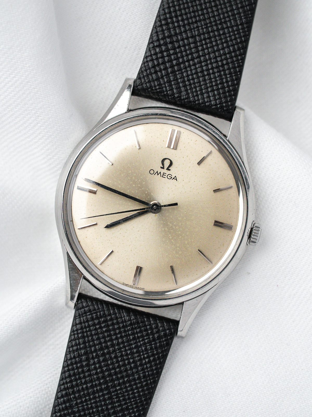 Vintage Omega watch with cream dial, steel case, and black textured strap